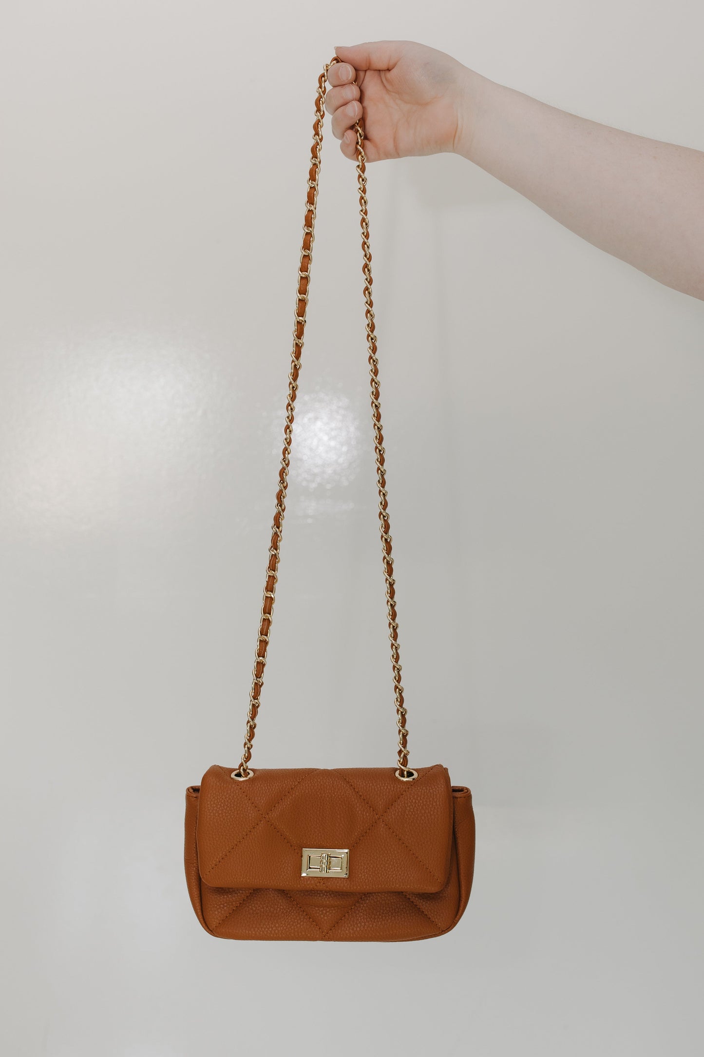 Brown handbag with a chain strap held by a hand against a light background