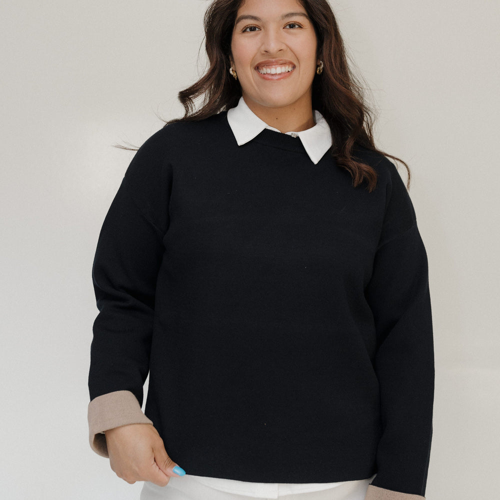 Woman wearing a black sweater with a white collar against a plain background