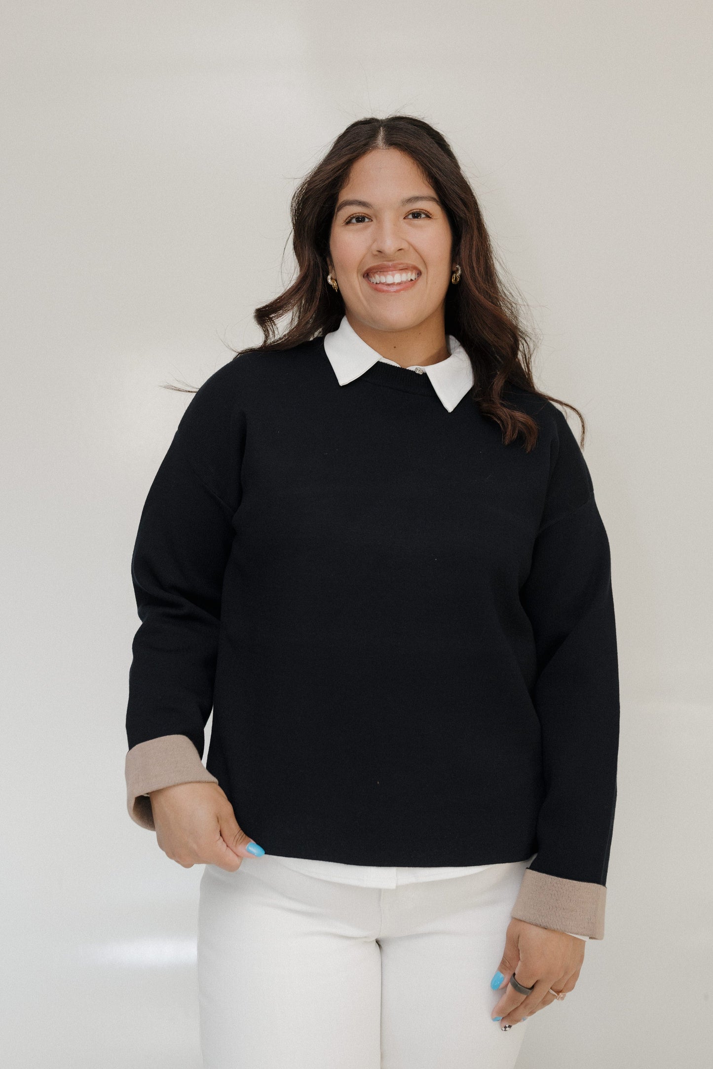 Woman wearing a black sweater with a white collar against a plain background