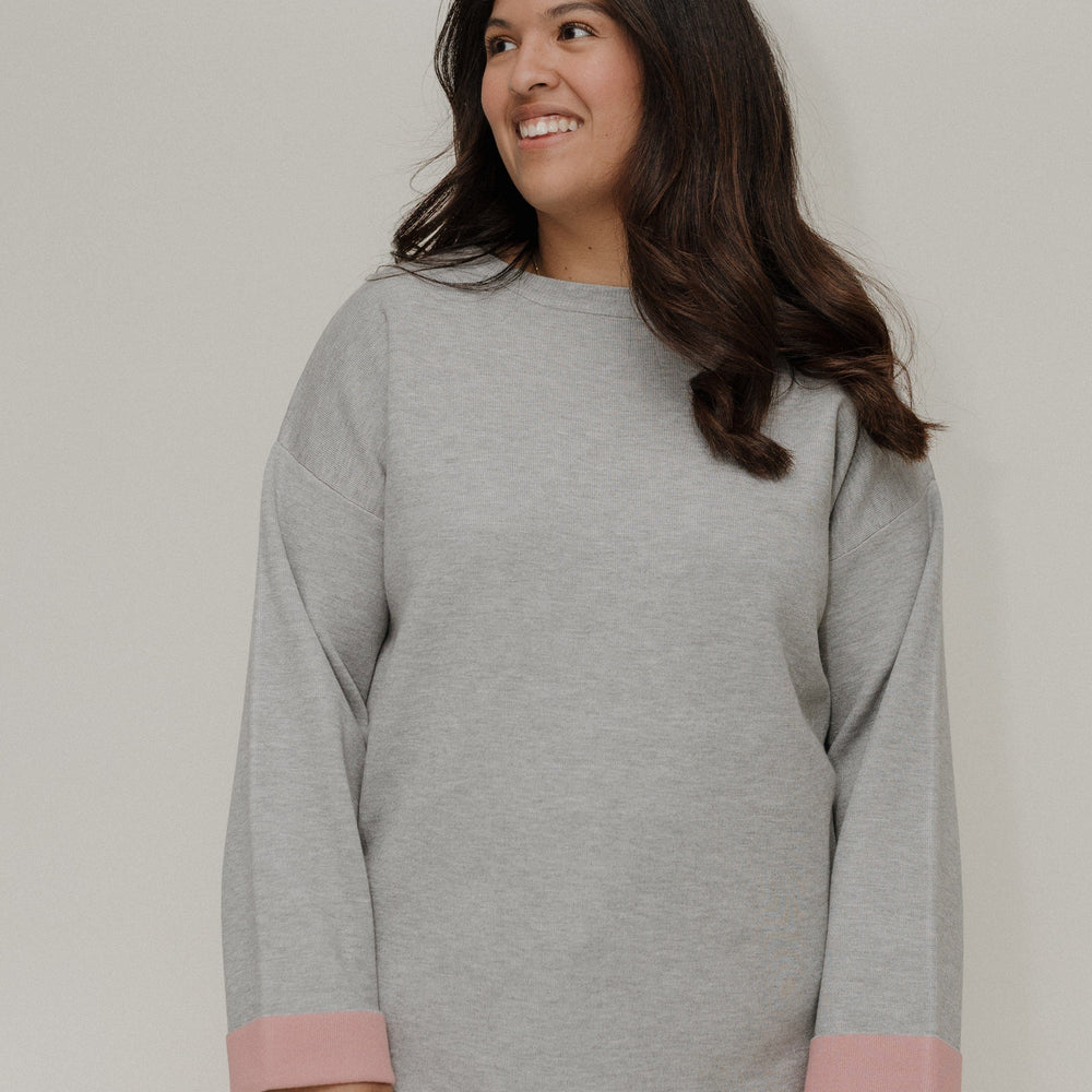 Woman wearing a gray sweater with pink cuffs and hem against a plain background