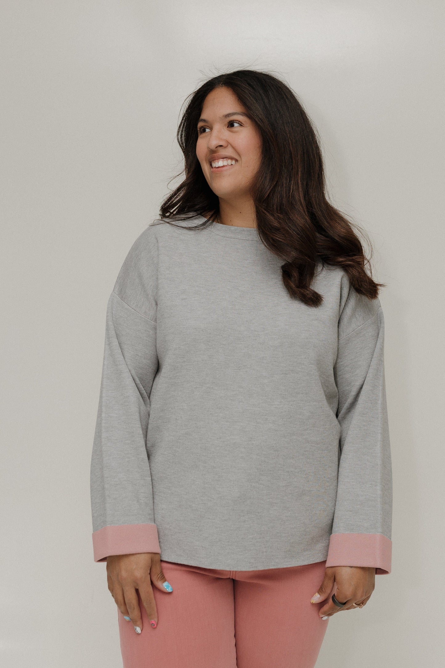Woman wearing a gray sweater with pink cuffs and hem against a plain background