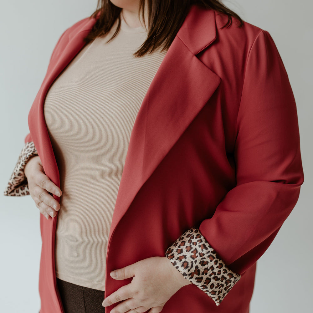 A person wearing the Oddi CLASSIC BLAZER IN LIPSTICK over a beige top and brown pants exudes confidence.