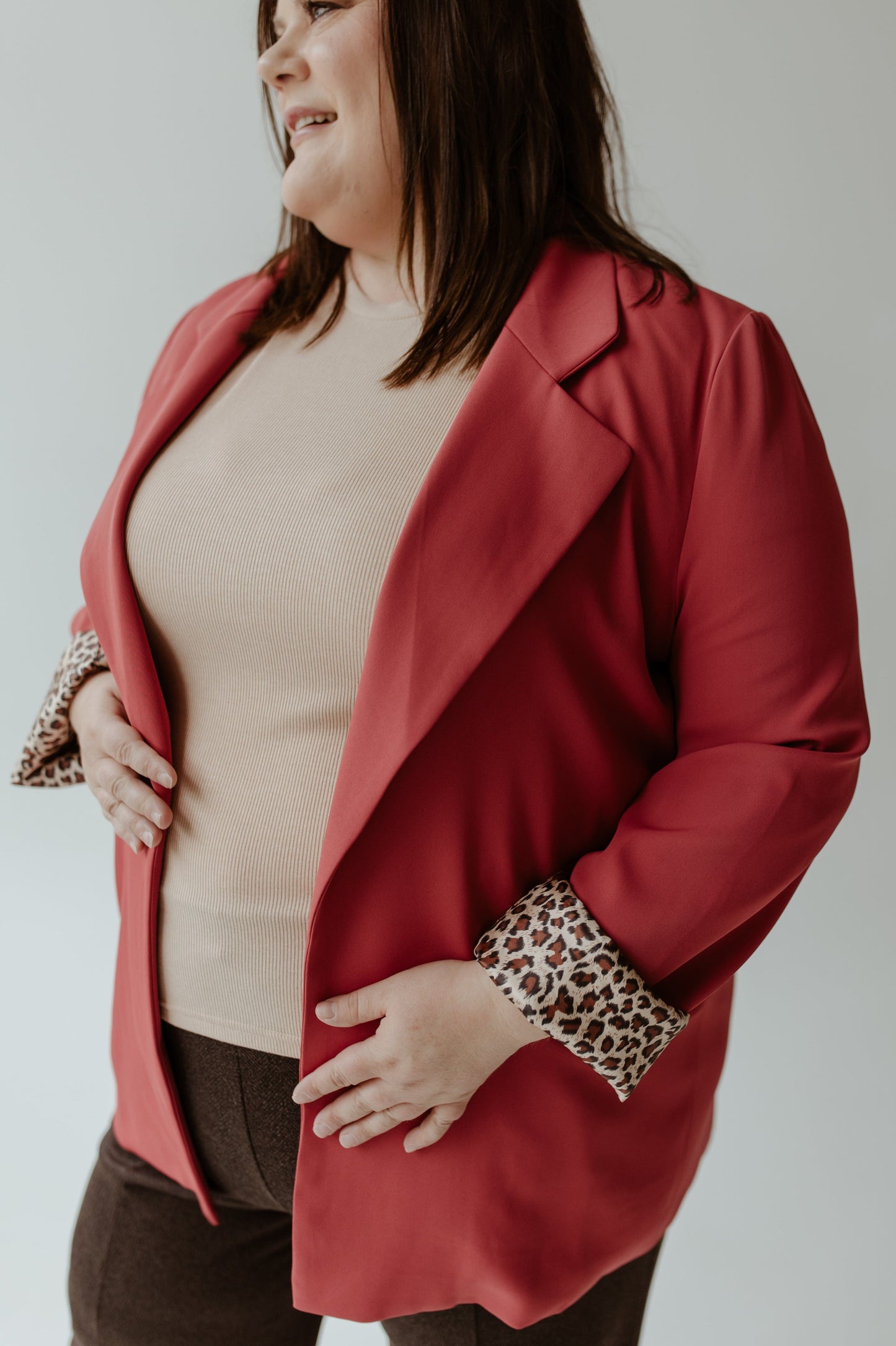 A person wearing the Oddi CLASSIC BLAZER IN LIPSTICK over a beige top and brown pants exudes confidence.