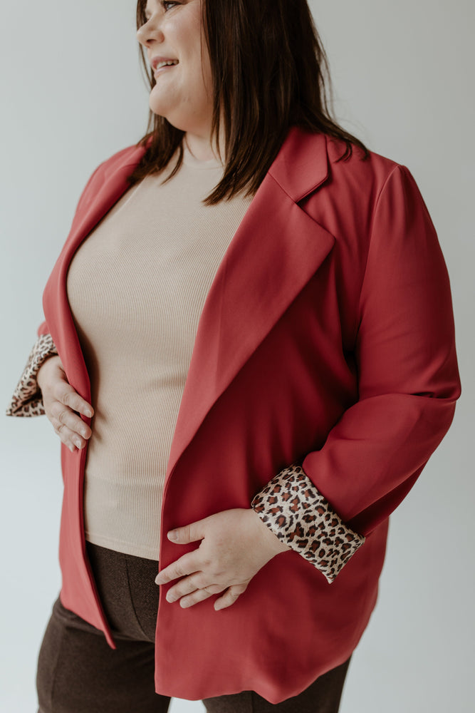 Wearing Oddi's CLASSIC BLAZER IN LIPSTICK paired with dark pants, an individual stands confidently against a plain background, their back to the camera.