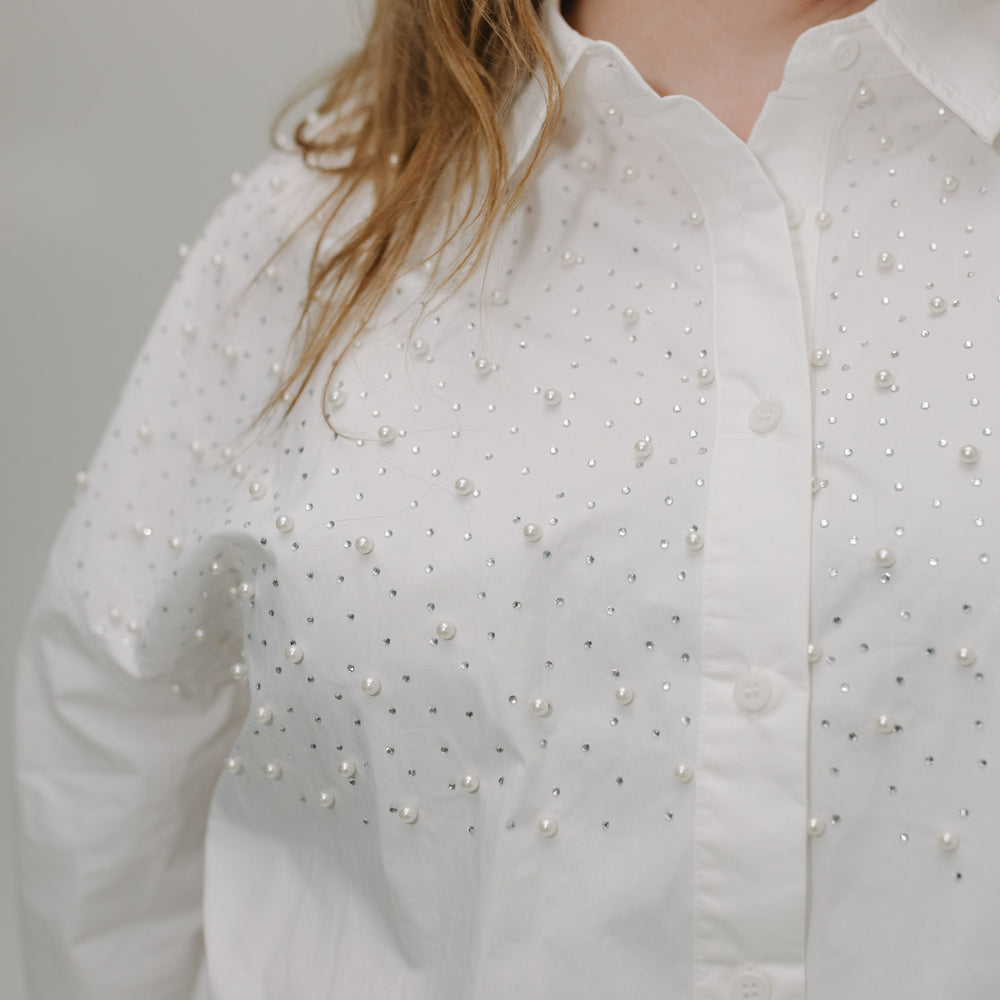 White shirt with pearl embellishments worn by a person against a neutral background