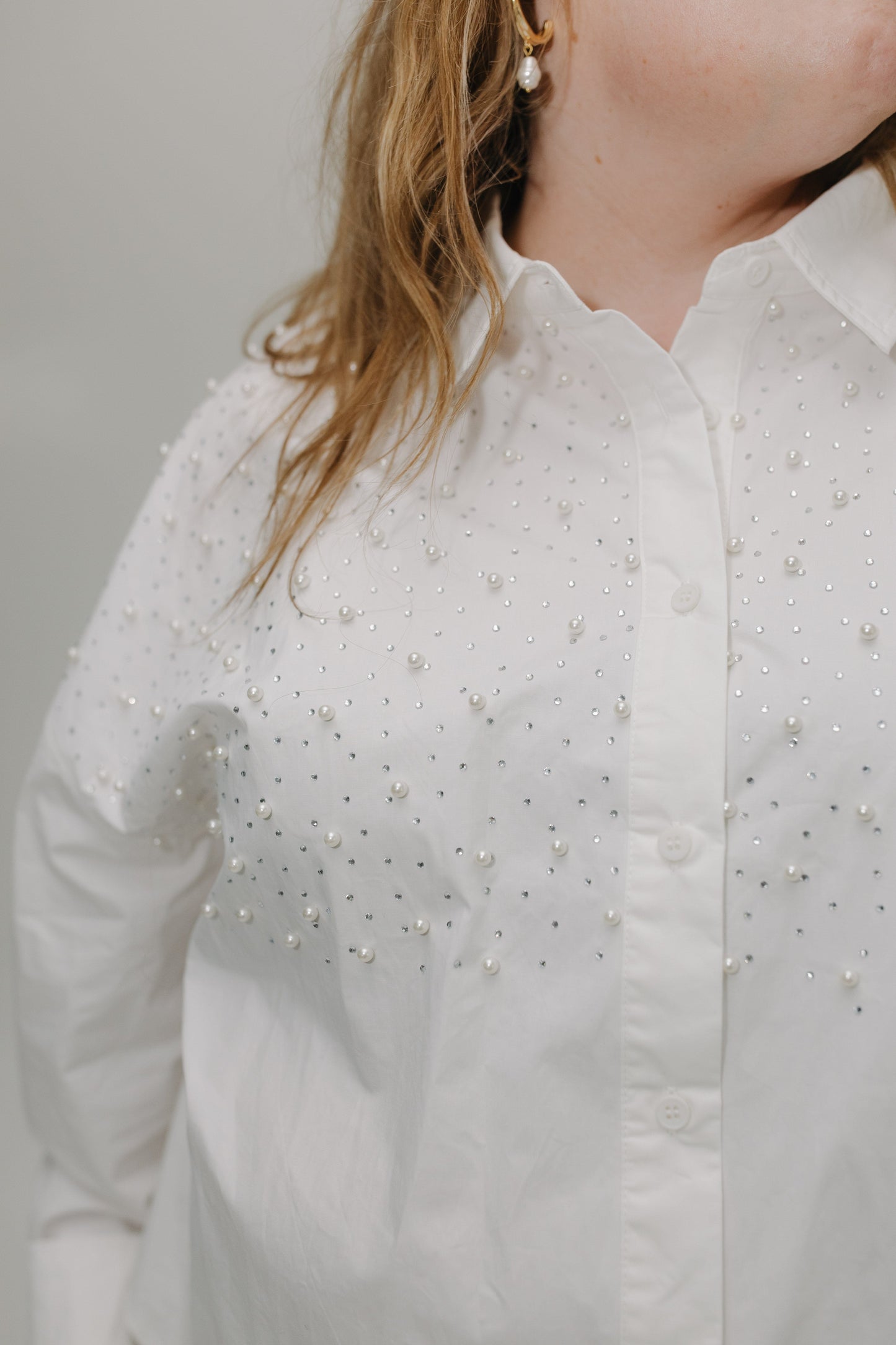 White shirt with pearl embellishments worn by a person against a neutral background