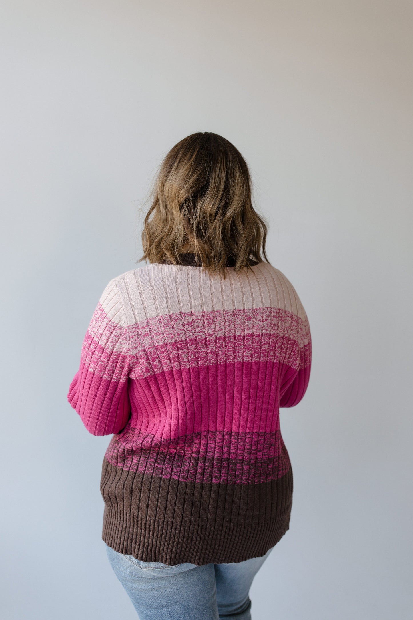 With their back turned, a person with wavy hair is enveloped in the cozy warmth of Yesta's Classic Cardigan with Color Fade in Pink.