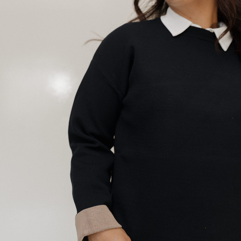 Woman wearing a black sweater with a white collar against a plain background