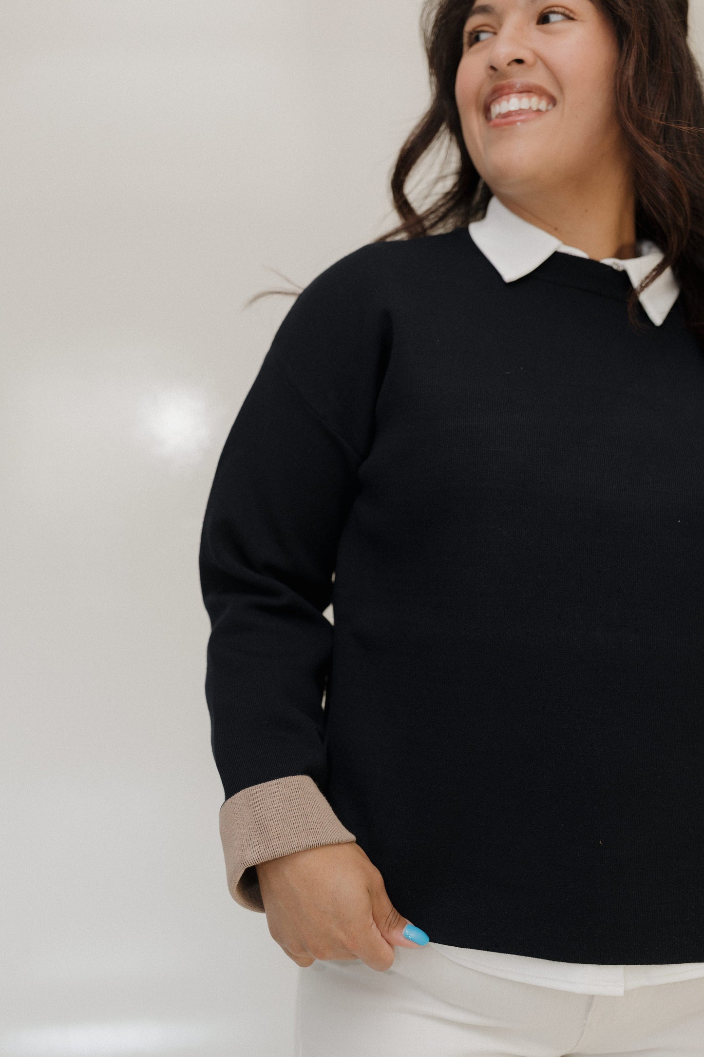 Woman wearing a black sweater with a white collar against a plain background
