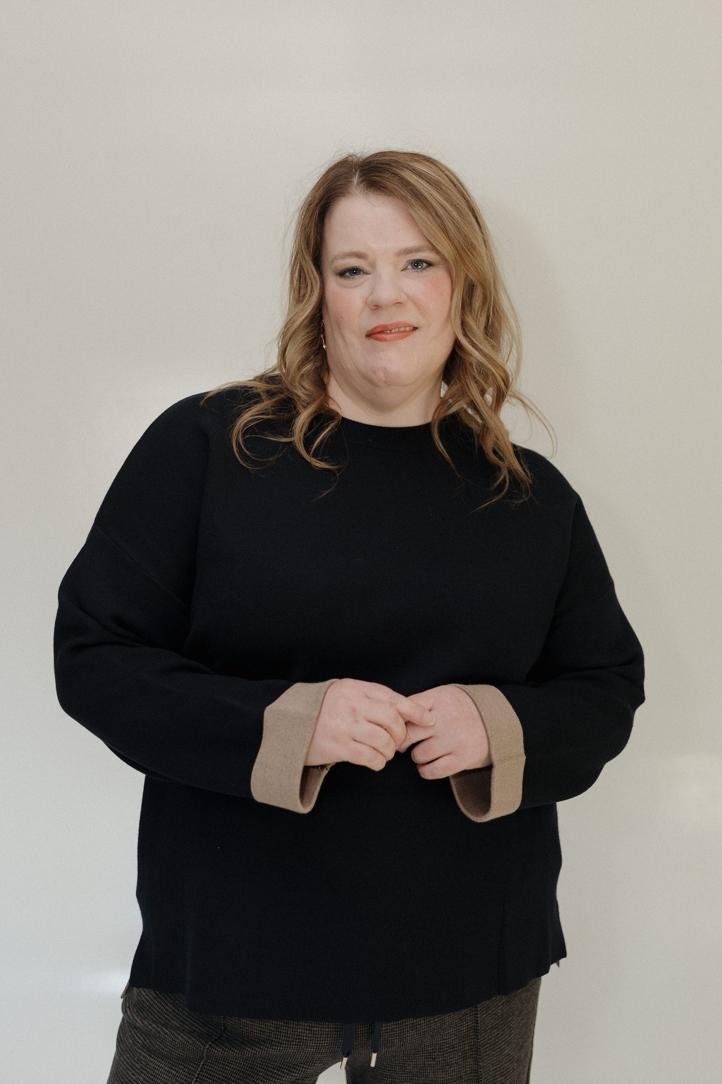Person wearing a black sweater with beige cuffs against a plain background