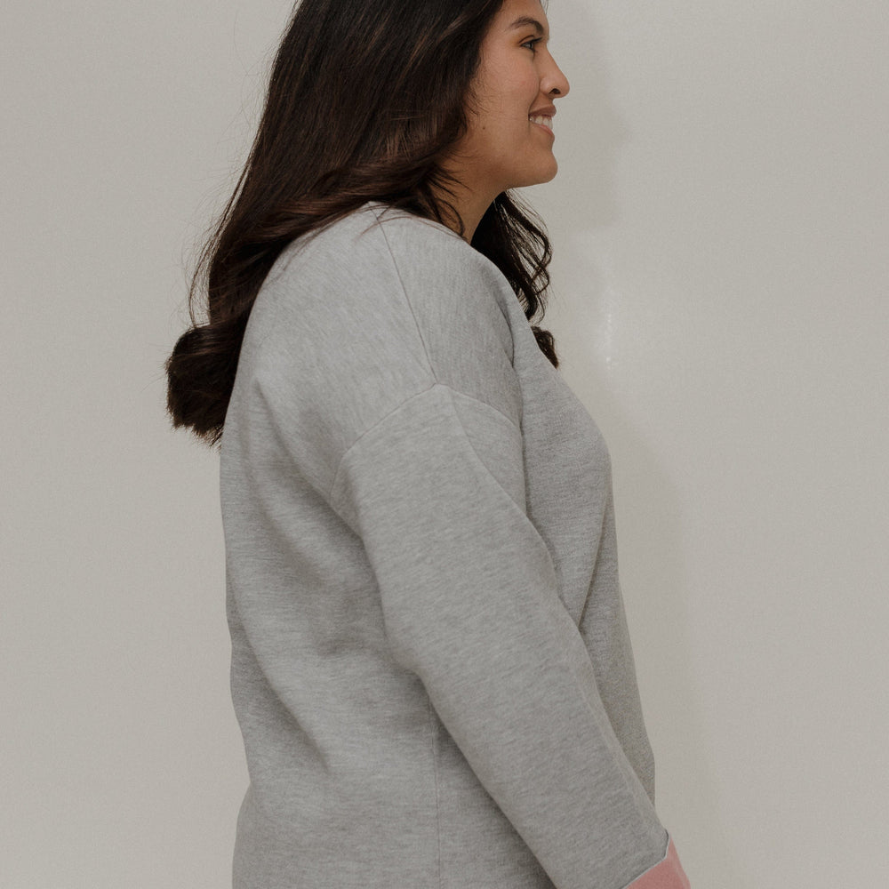 Woman wearing a gray sweater and pink pants against a plain background