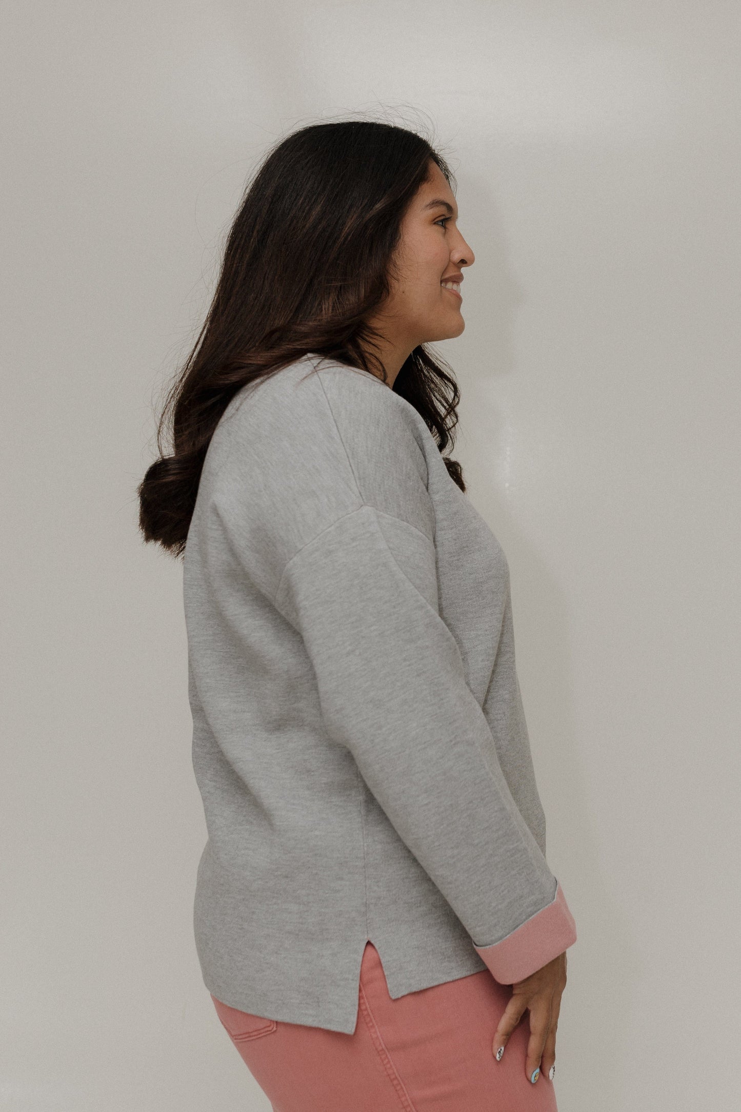 Woman wearing a gray sweater and pink pants against a plain background