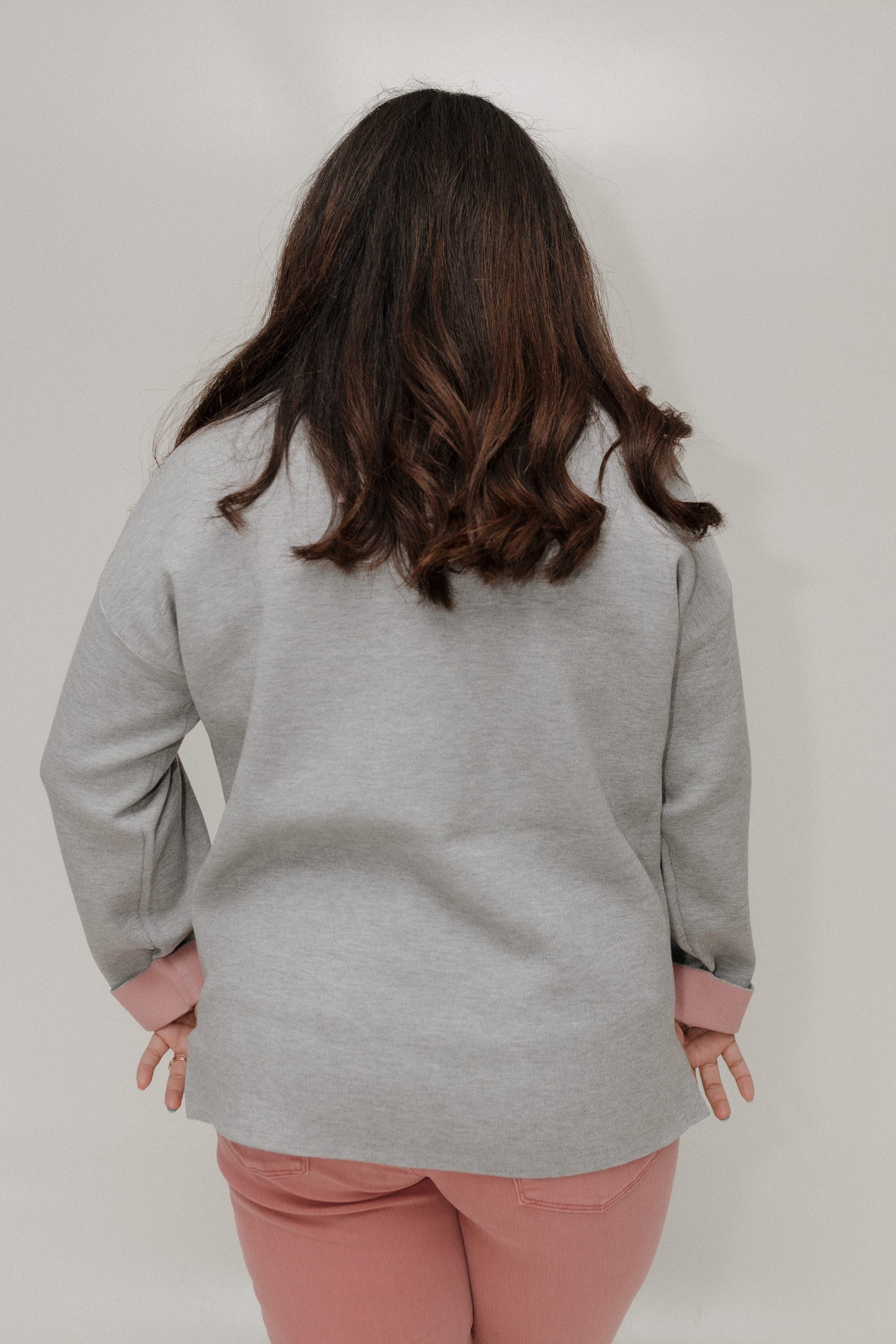 Person wearing a gray sweater and pink pants against a plain background