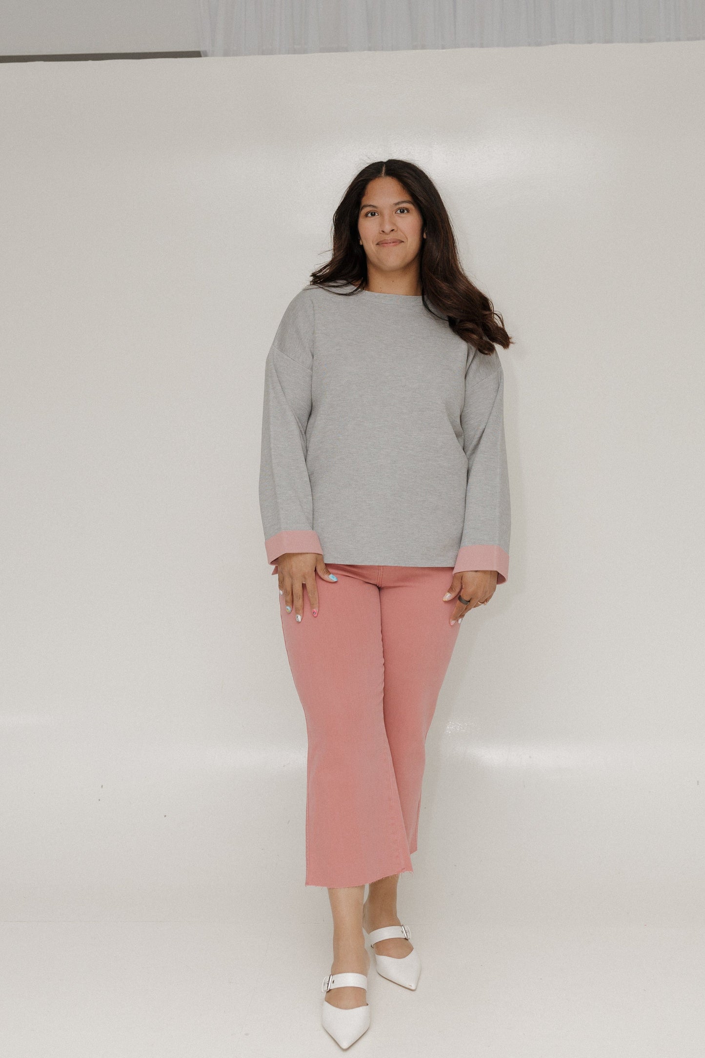 Woman wearing a gray sweater and pink pants against a white background
