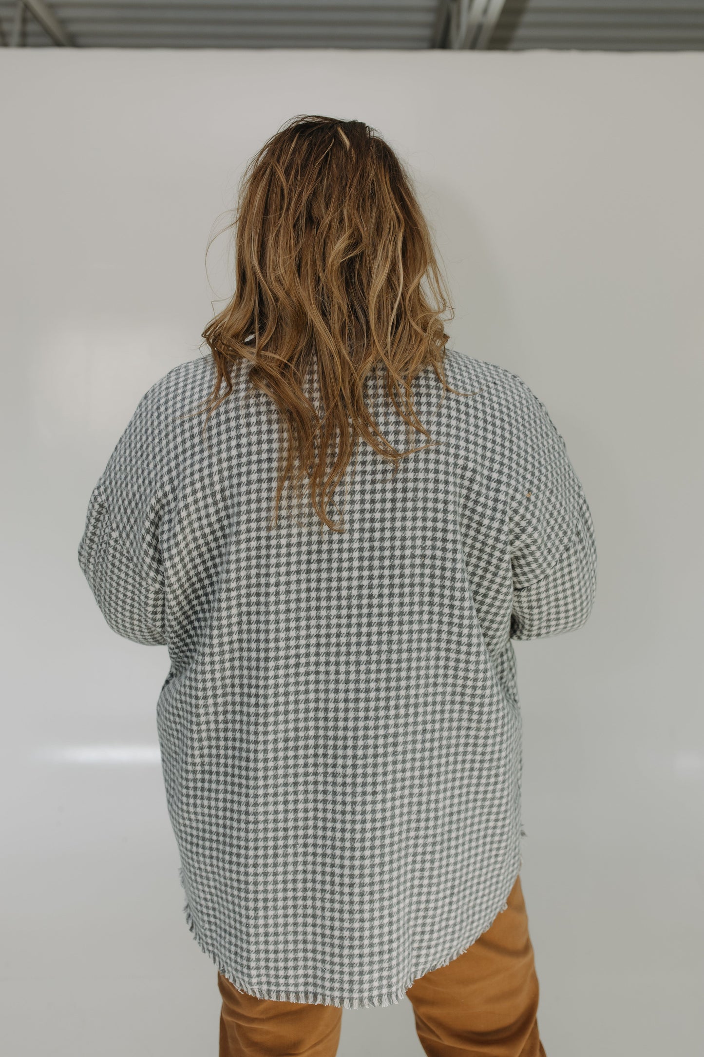 Person wearing a checkered shirt and brown pants standing against a white wall