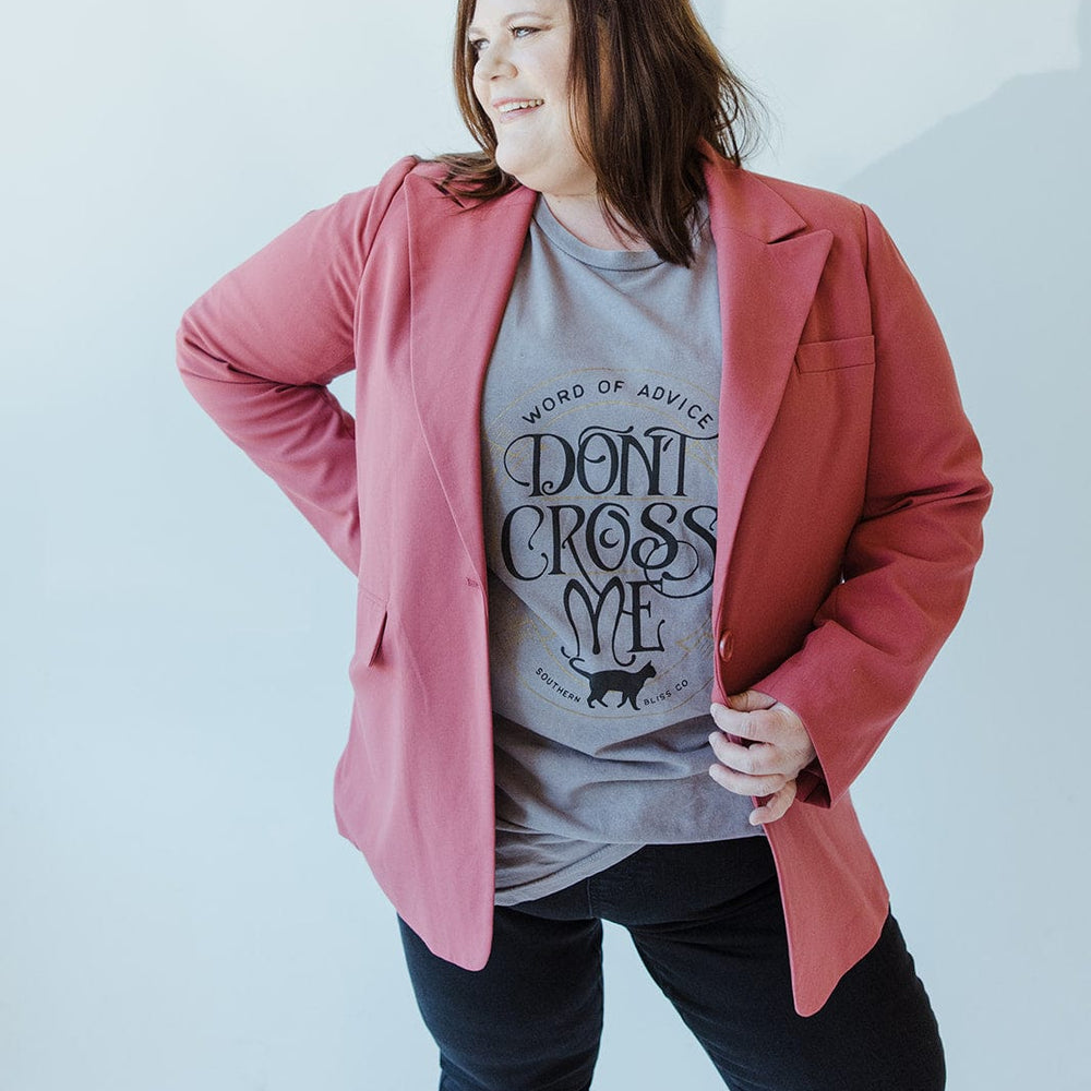 A woman makes a timelessly chic statement by wearing her Yesta CLASSIC NOTCHED BLAZER in pink over a graphic T-shirt that boldly declares "Don't Cross Me," set against a light background.