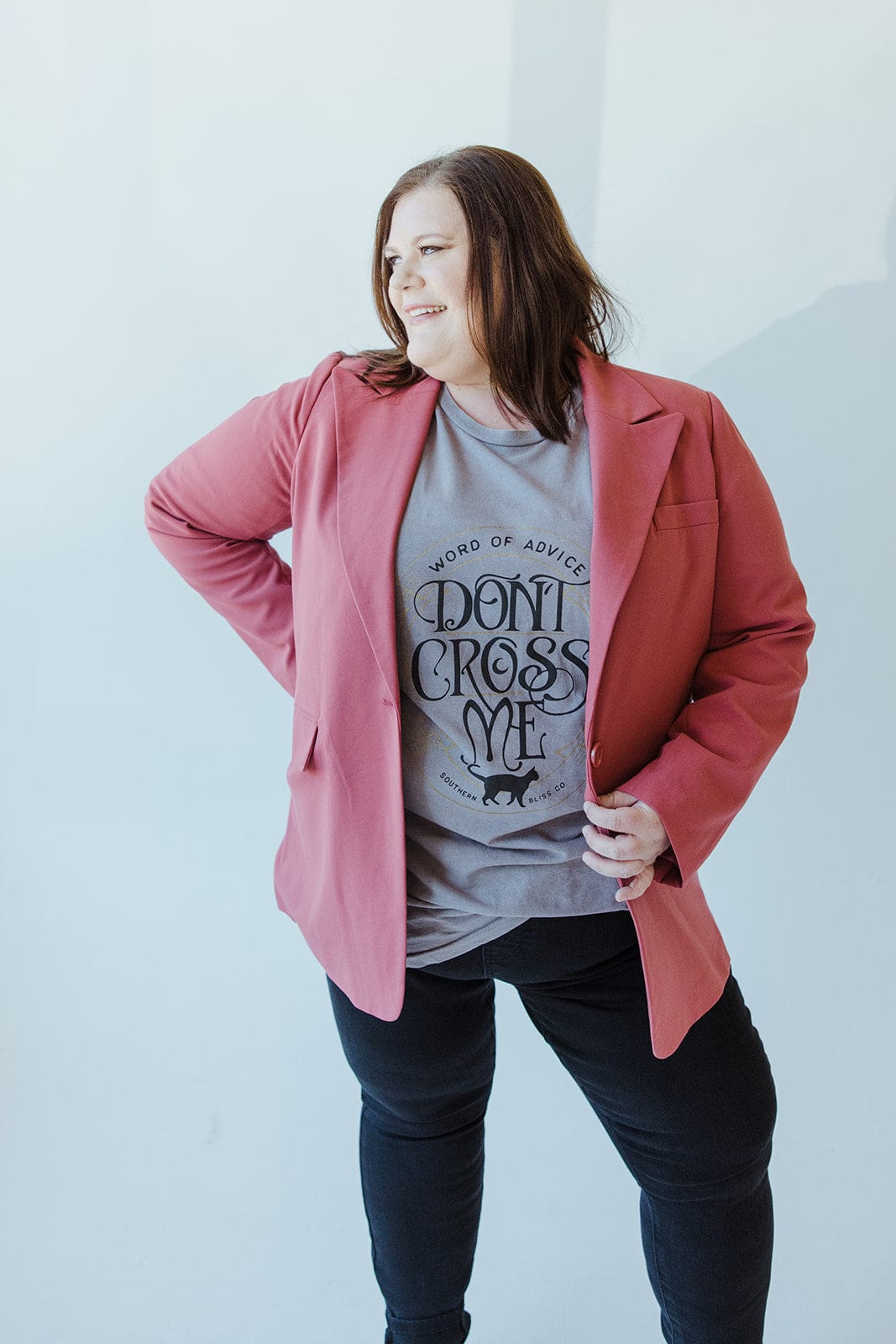 A woman makes a timelessly chic statement by wearing her Yesta CLASSIC NOTCHED BLAZER in pink over a graphic T-shirt that boldly declares "Don't Cross Me," set against a light background.