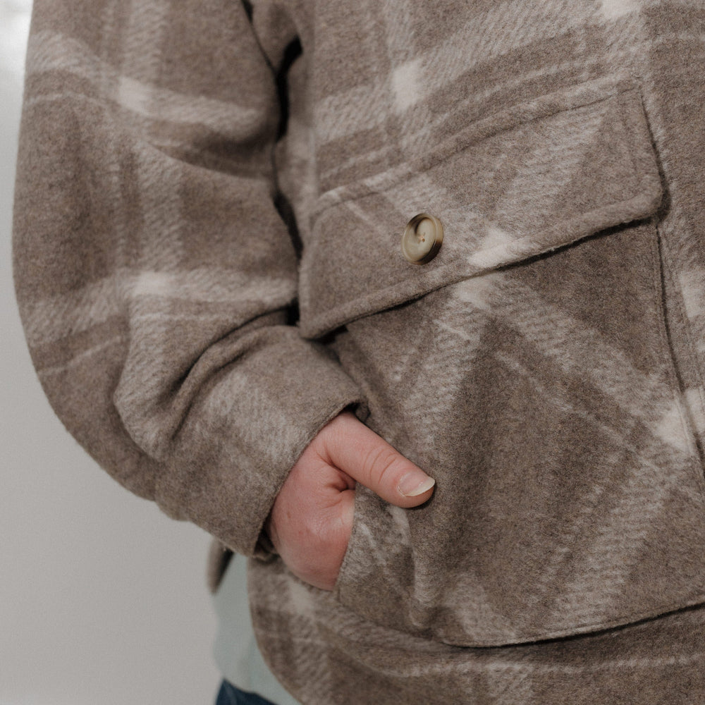 Close-up of a person wearing a brown plaid jacket with a pocket.