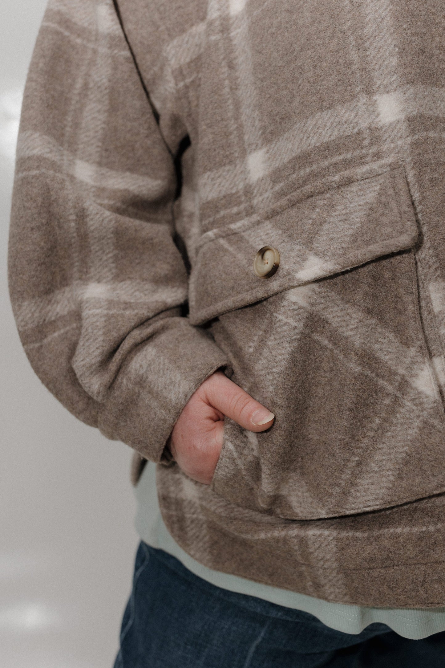 Close-up of a person wearing a brown plaid jacket with a pocket.