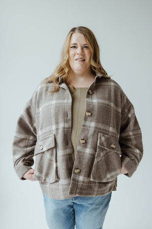 A person with long hair wearing the Yesta Classic Shacket in earth tones and jeans stands against a plain background.