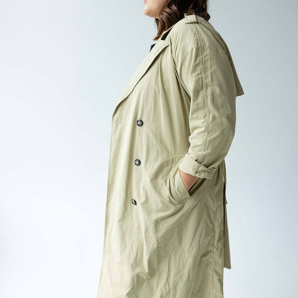 A person stands against a plain white background, hands tucked into their pockets, showcasing the Yesta CLASSIC TRENCH COAT in beige. This coat features water-resistant fabric and double-breasted buttons, adding both style and functionality to the timeless ensemble.
