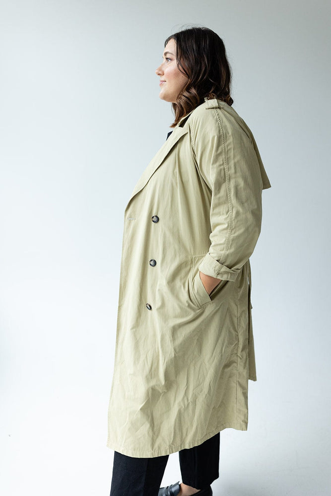 A person stands against a plain white background, hands tucked into their pockets, showcasing the Yesta CLASSIC TRENCH COAT in beige. This coat features water-resistant fabric and double-breasted buttons, adding both style and functionality to the timeless ensemble.