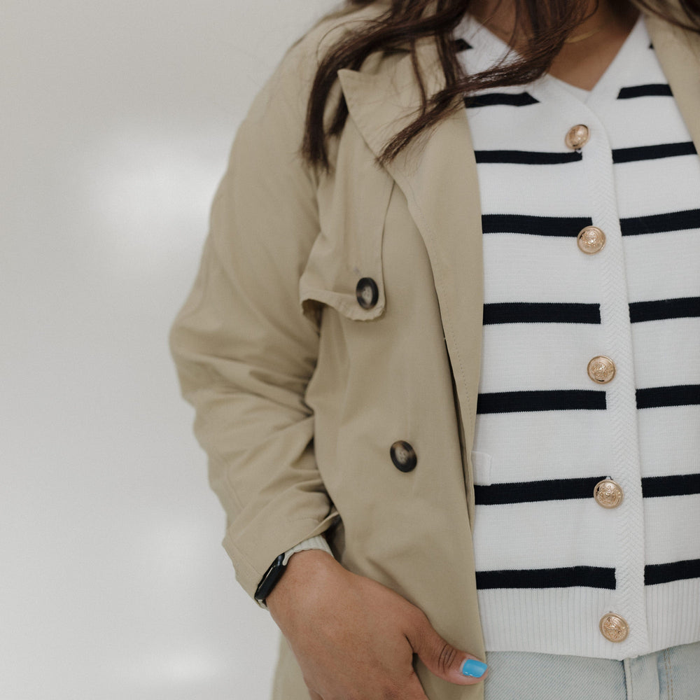 Person wearing a beige trench coat over a striped shirt with a neutral background