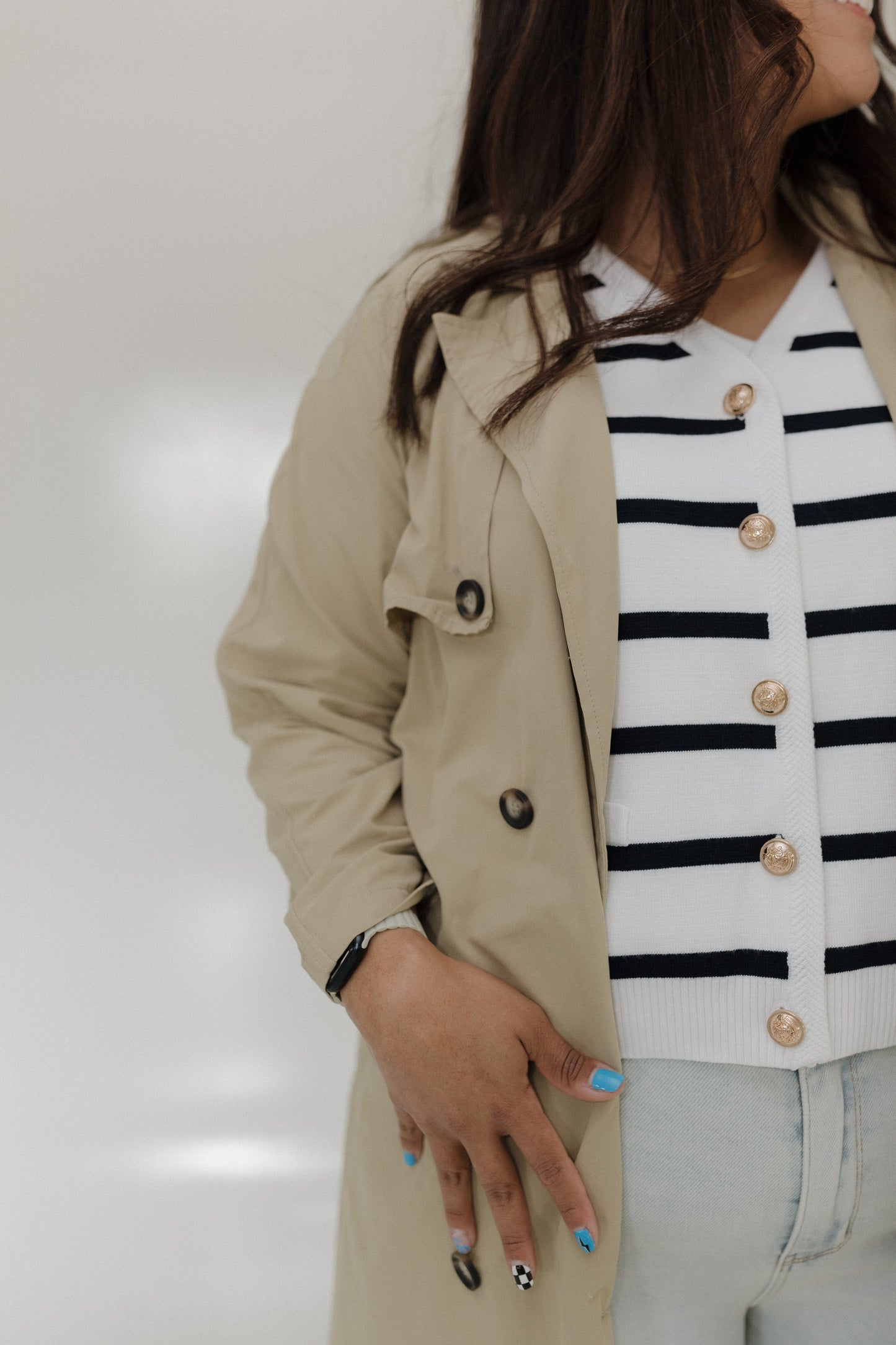 Person wearing a beige trench coat over a striped shirt with a neutral background
