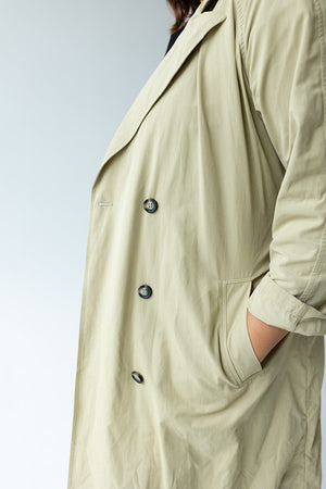 A person wearing the CLASSIC TRENCH COAT by Yesta, which features double-breasted buttons and is made from water-resistant fabric, stands with their hand in the pocket, shown from the side.