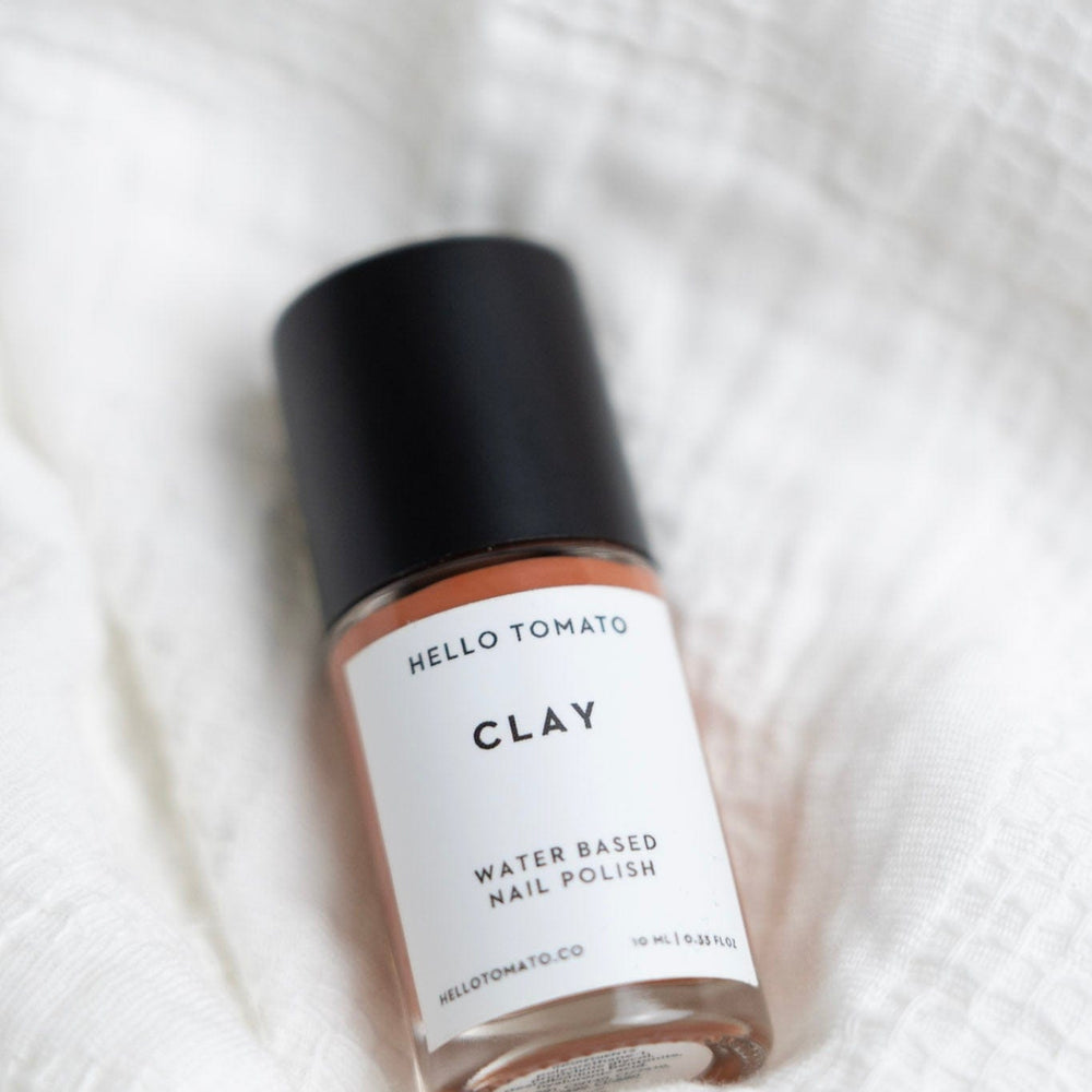 Bottle of Hello Tomato CLAY water-based nail polish on a white textured background