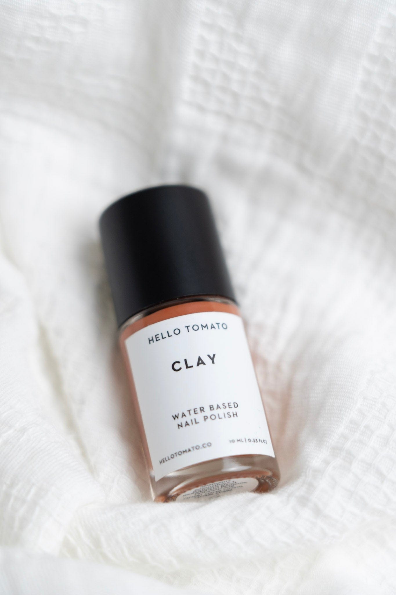 Bottle of Hello Tomato CLAY water-based nail polish on a white textured background