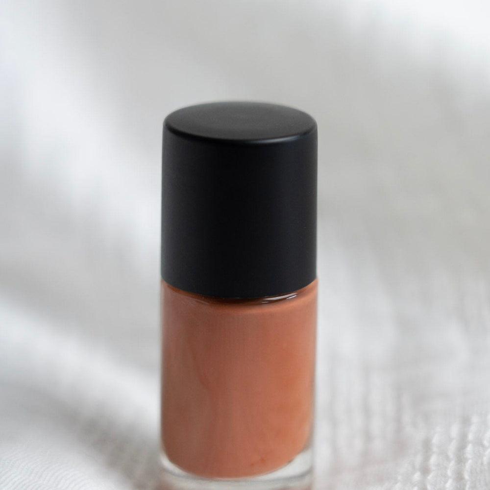 Cosmetic bottle with a black cap and clay nail polish on a textured white background