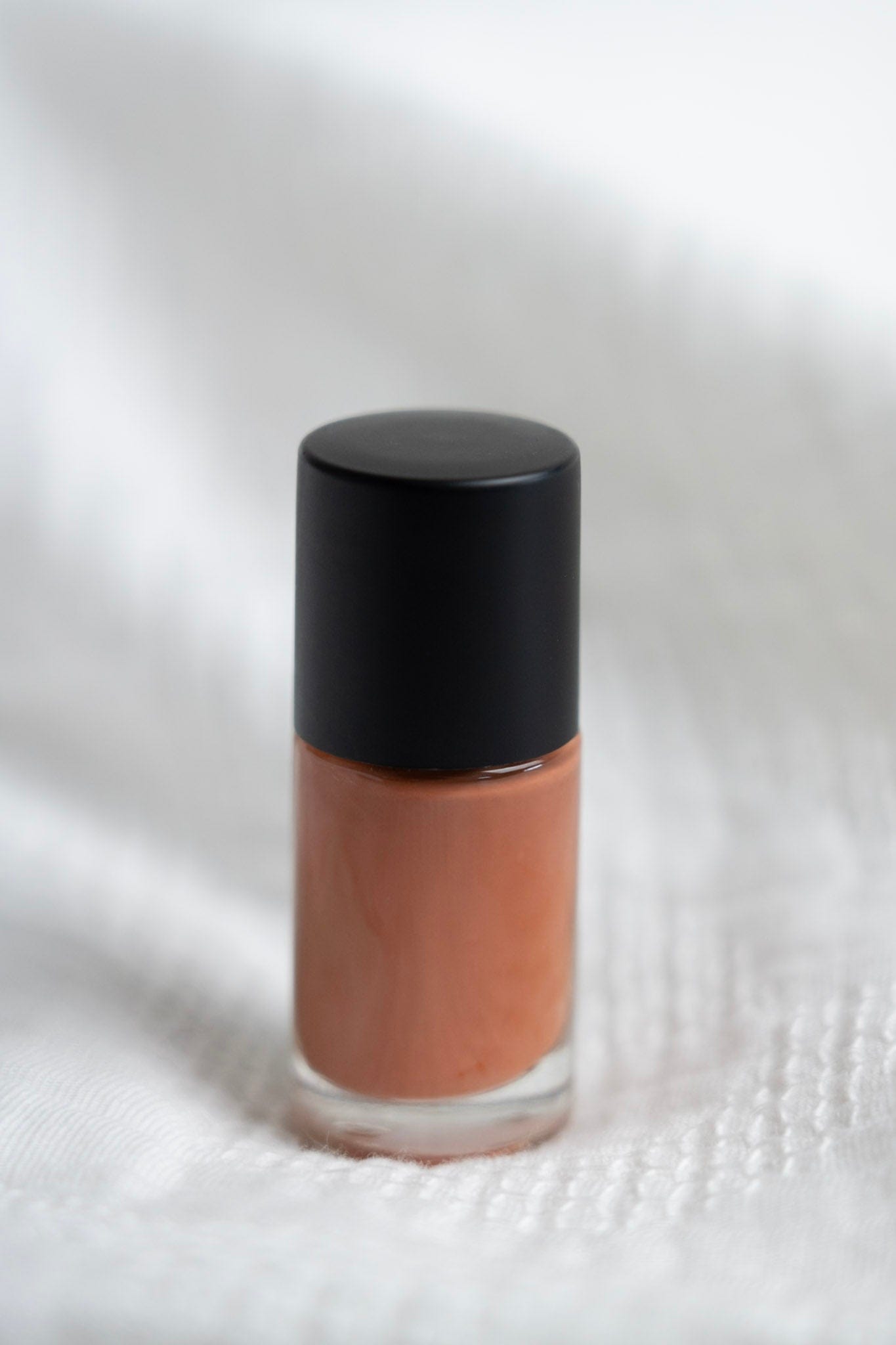 Cosmetic bottle with a black cap and clay nail polish on a textured white background