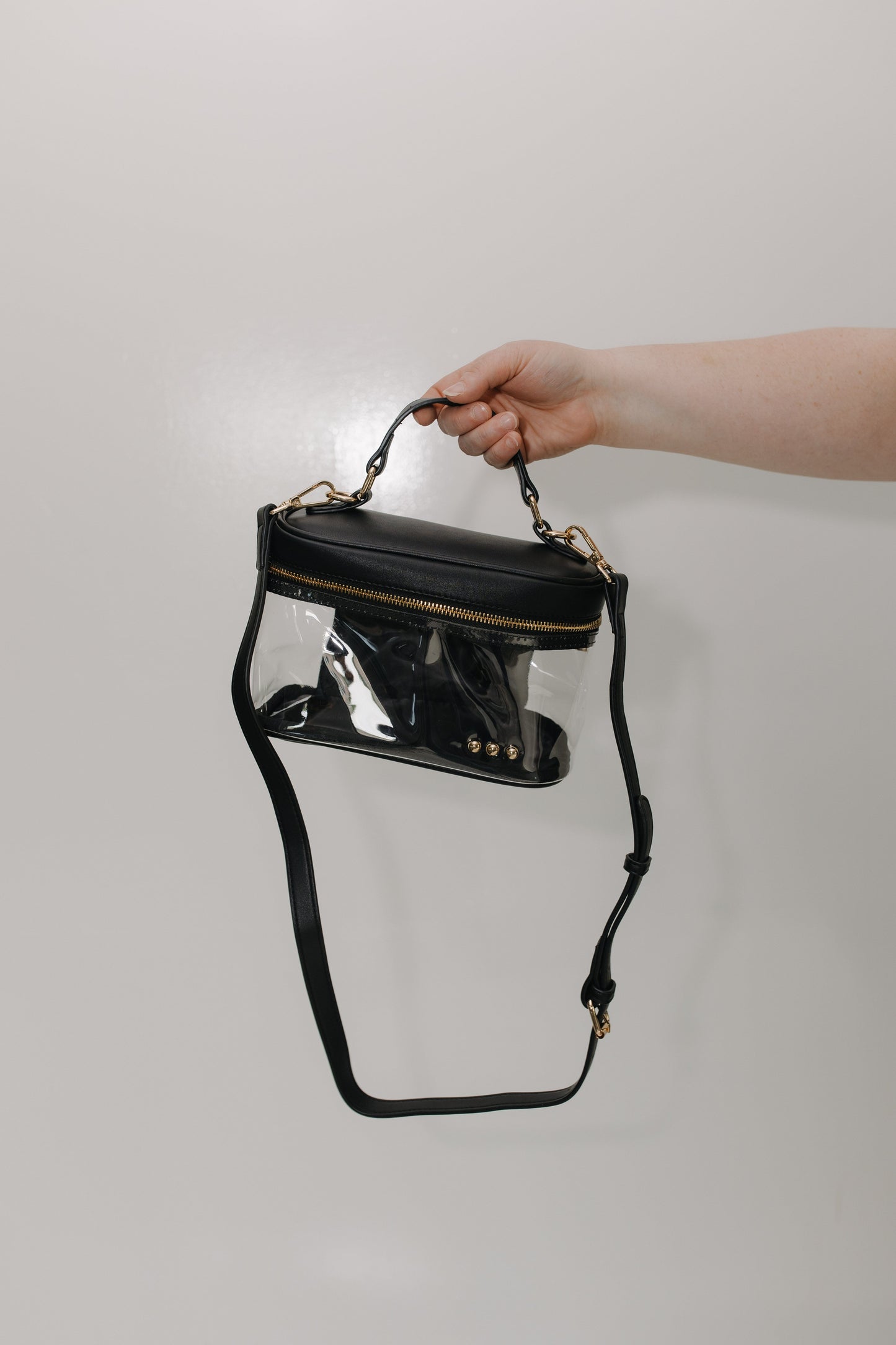 Black handbag with clear front held by a hand against a light gray background