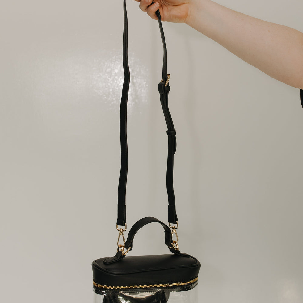 Black handbag with clear bottom section held by a hand against a neutral background