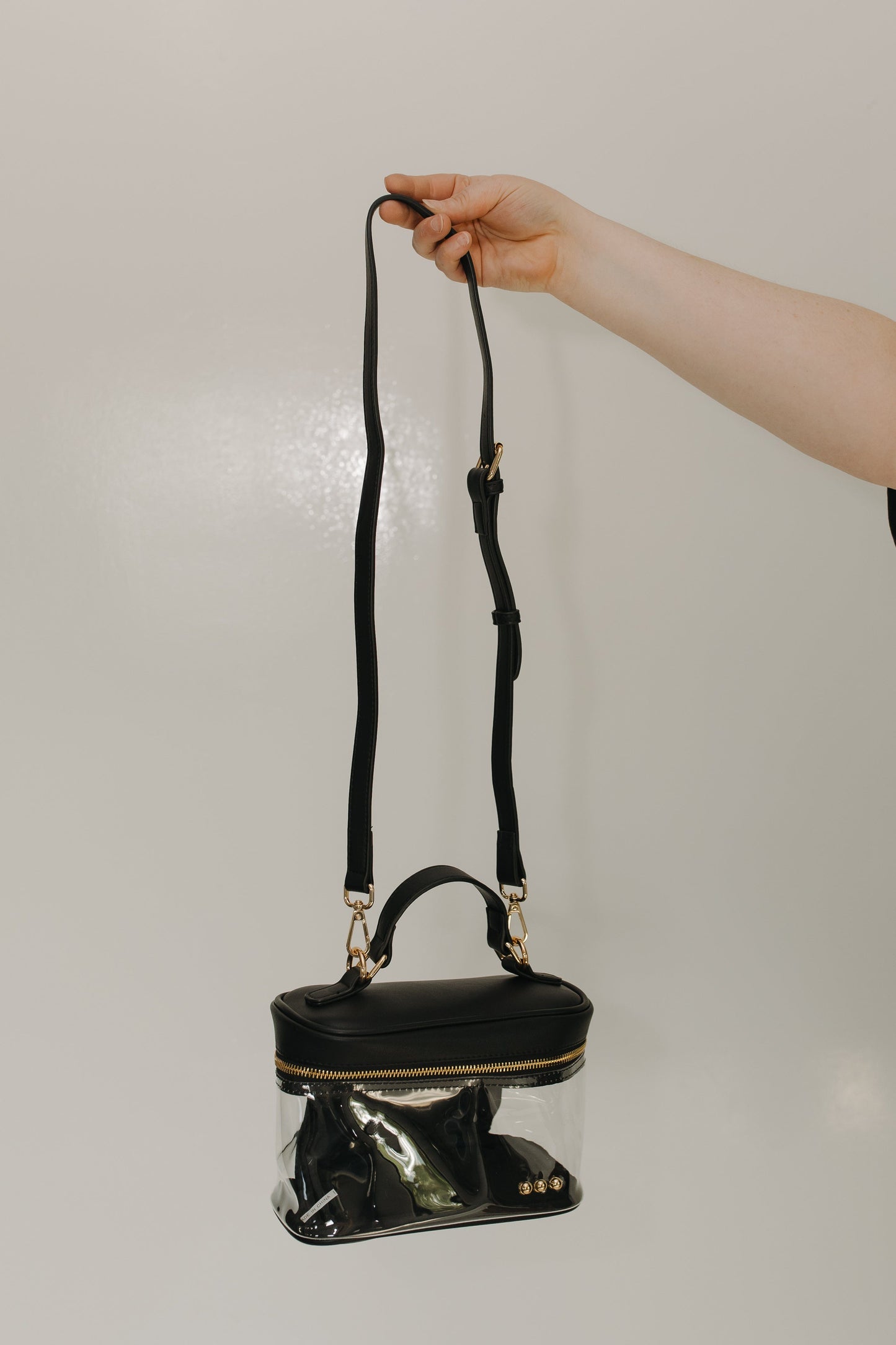 Black handbag with clear bottom section held by a hand against a neutral background