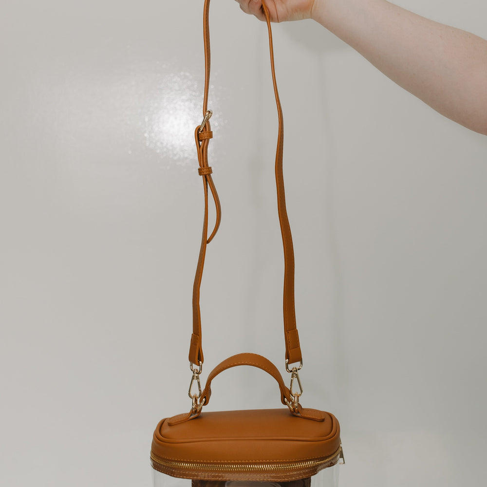 Hand holding a brown handbag with a clear pouch on a light gray background