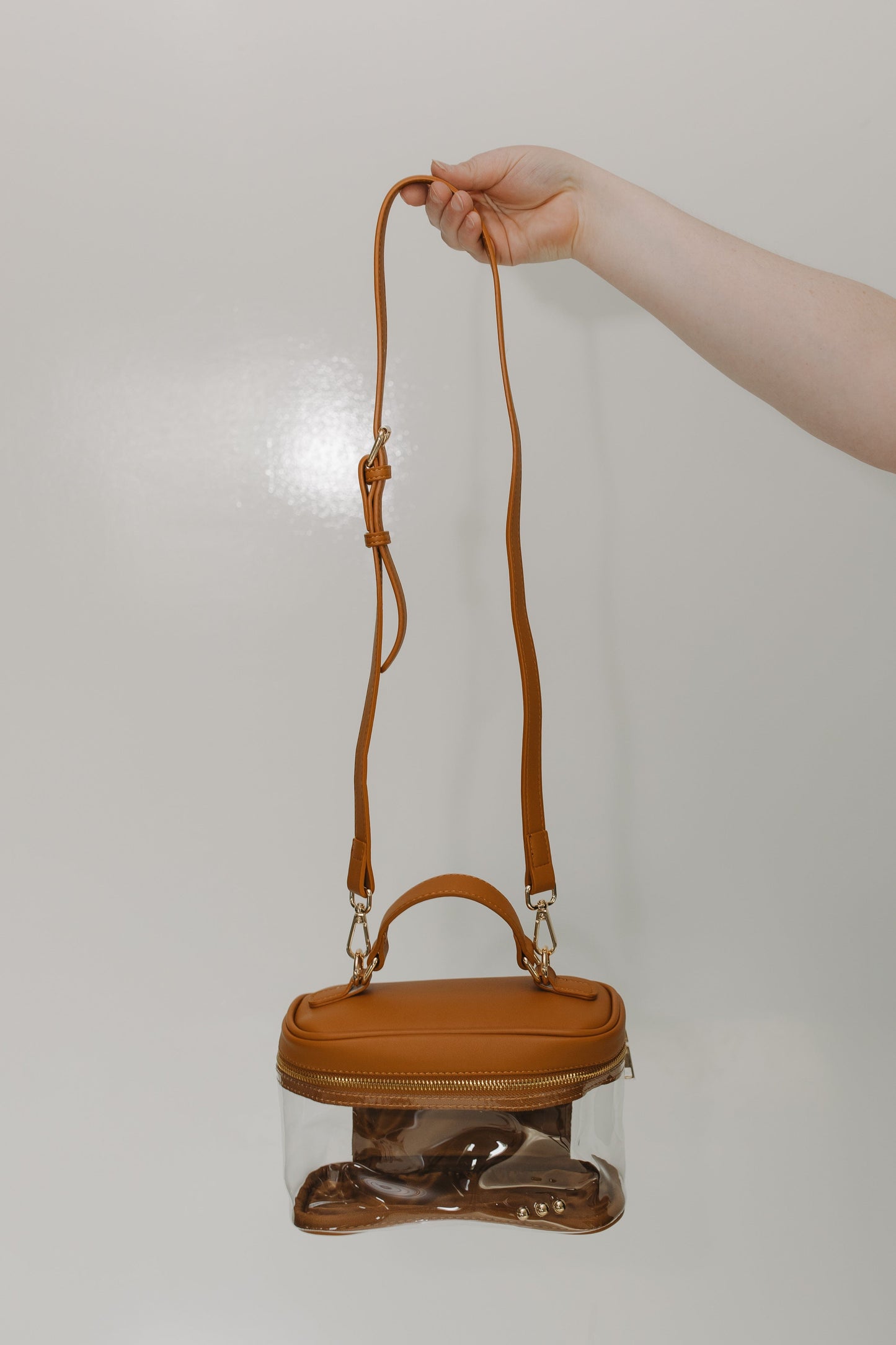 Hand holding a brown handbag with a clear pouch on a light gray background