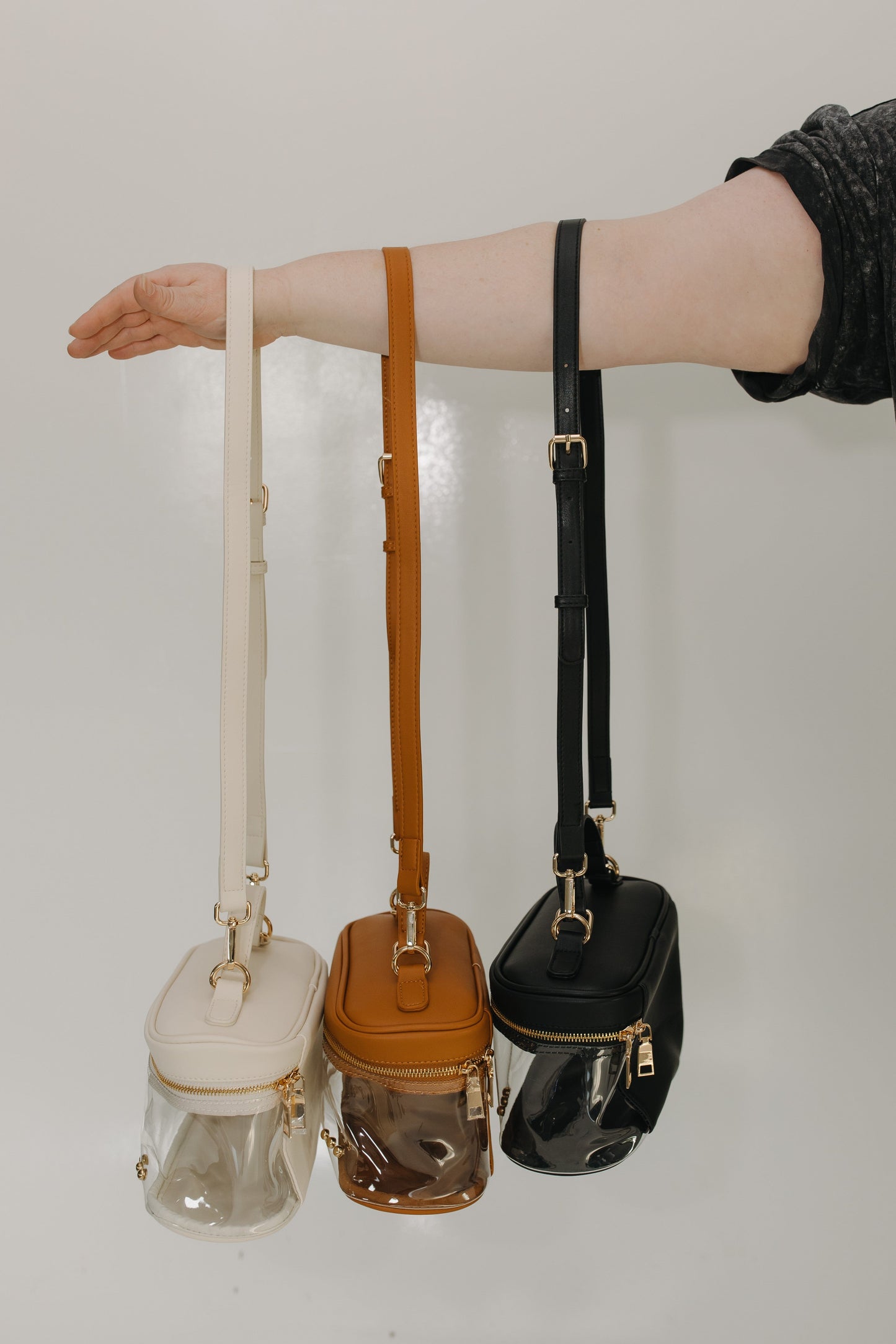 Three small handbags with different straps held by a person against a neutral background