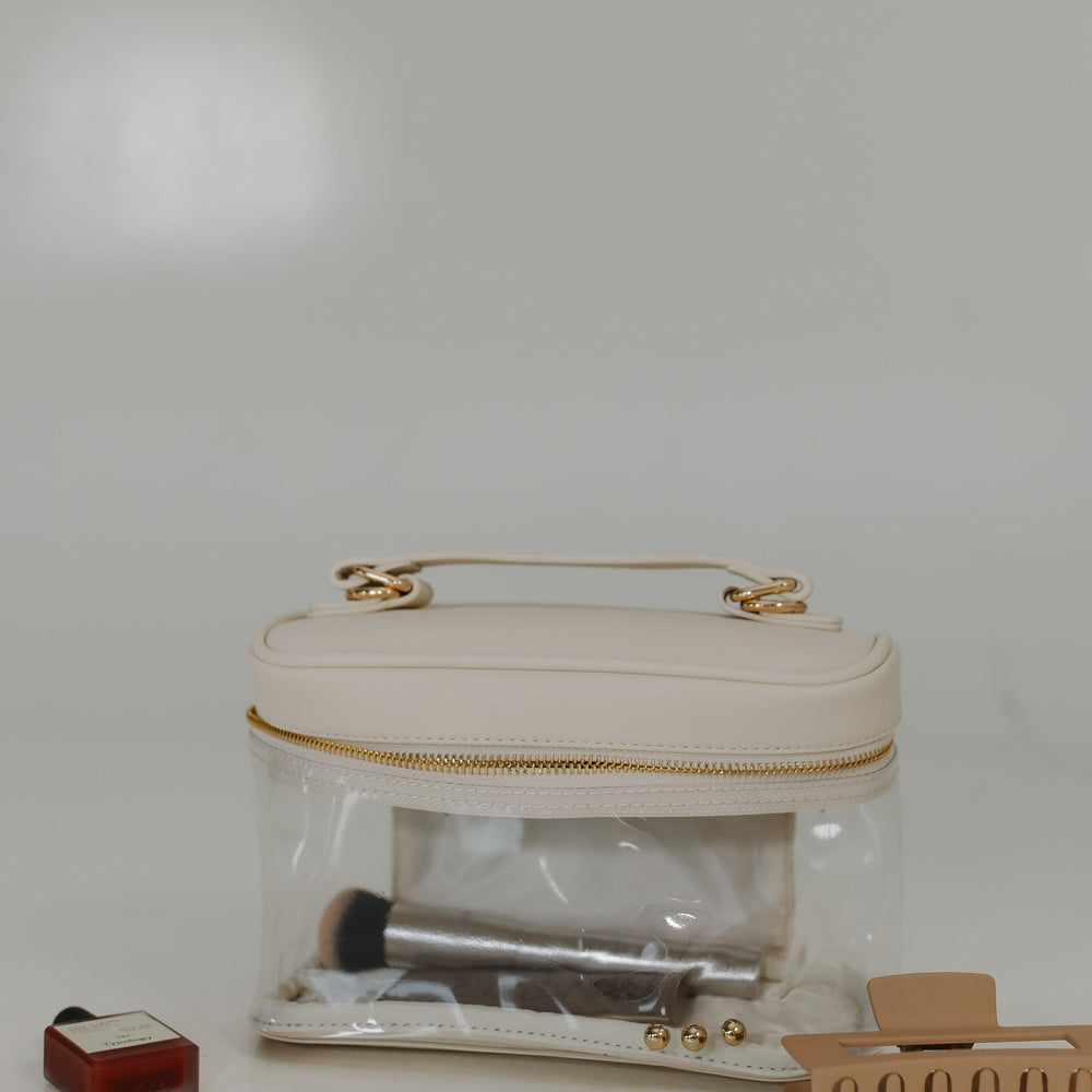 Clear plastic bag with gold handle, makeup items, and a hair clip on a white background