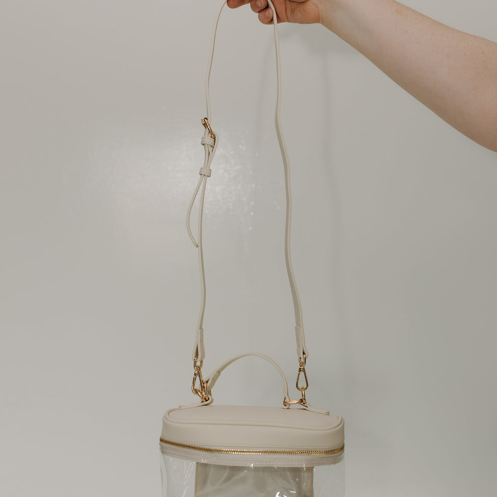 Clear handbag with gold accents held by a hand against a plain background