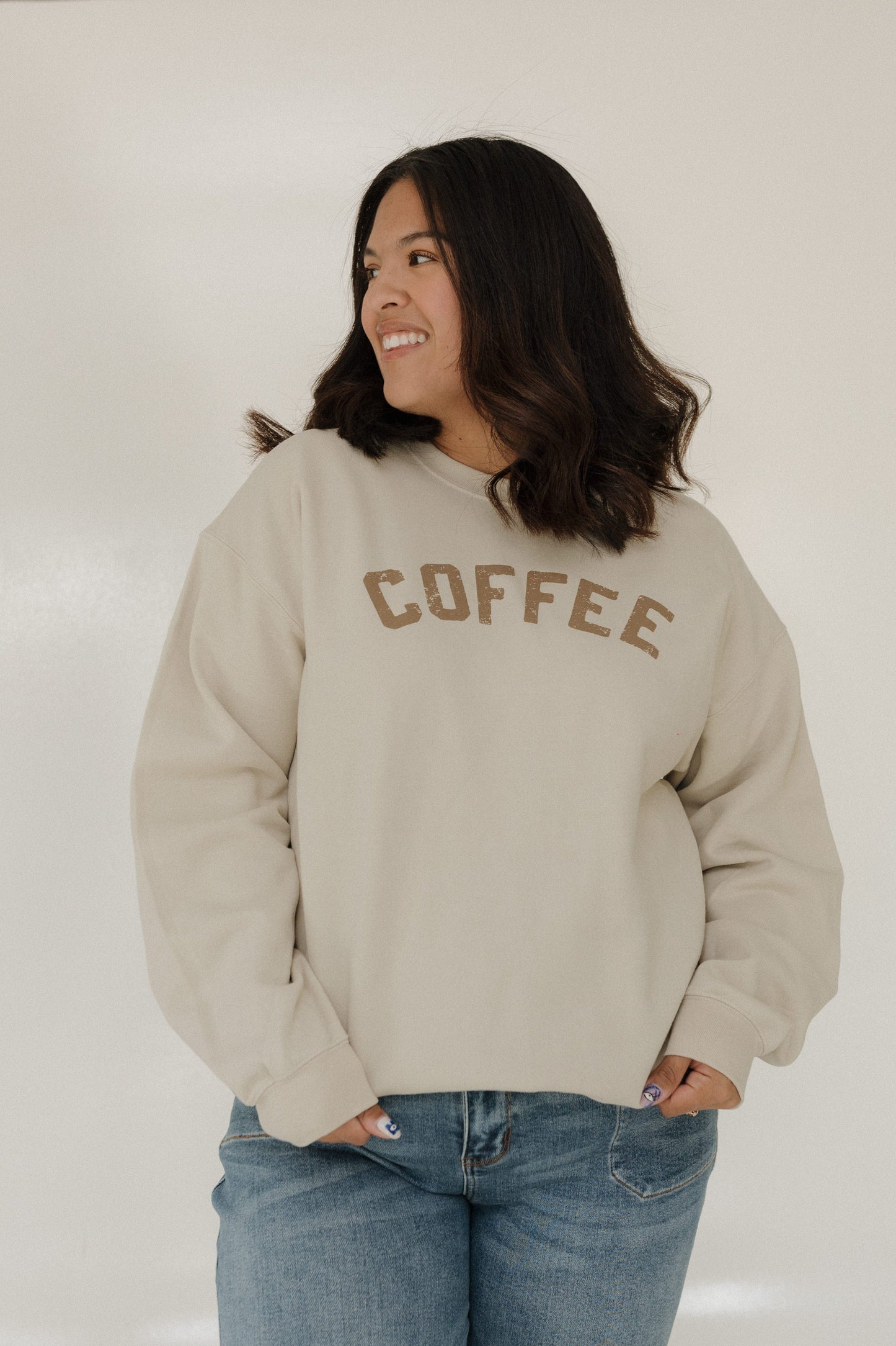 Person wearing a beige sweatshirt with 'COFFEE' text on a plain background