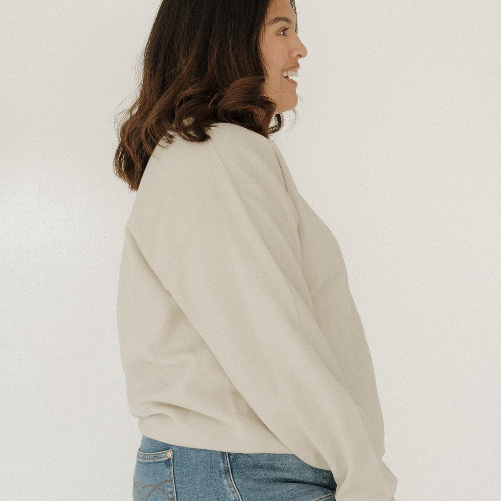 Woman wearing a beige sweater and blue jeans against a white background