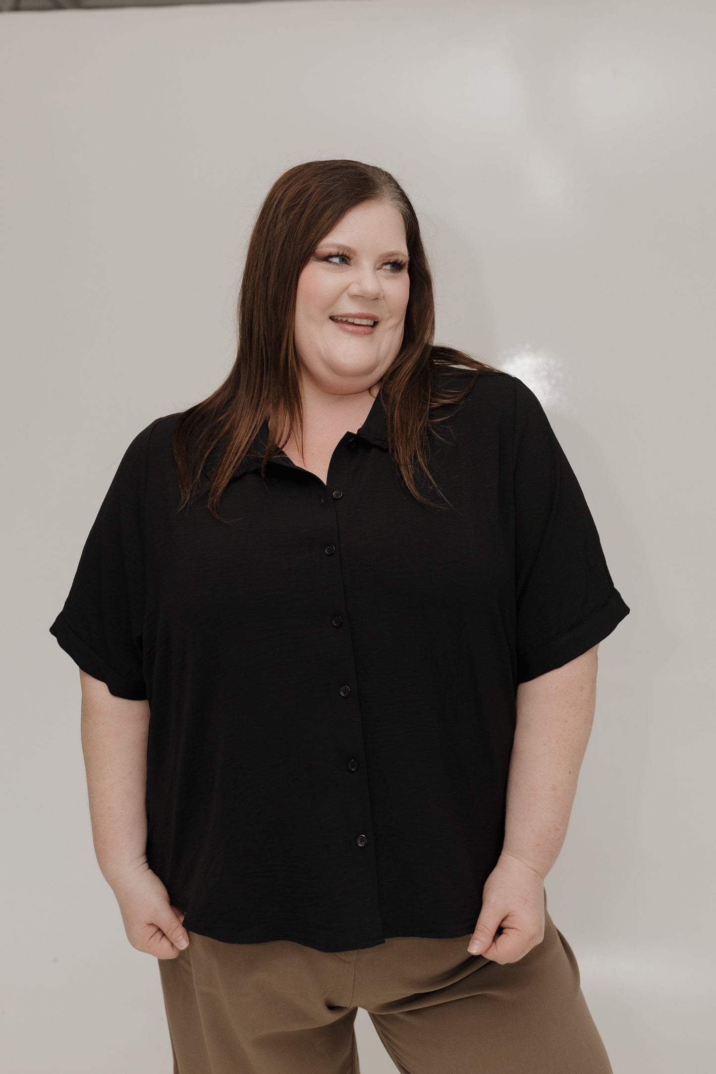 Person wearing a black shirt and brown pants against a plain background