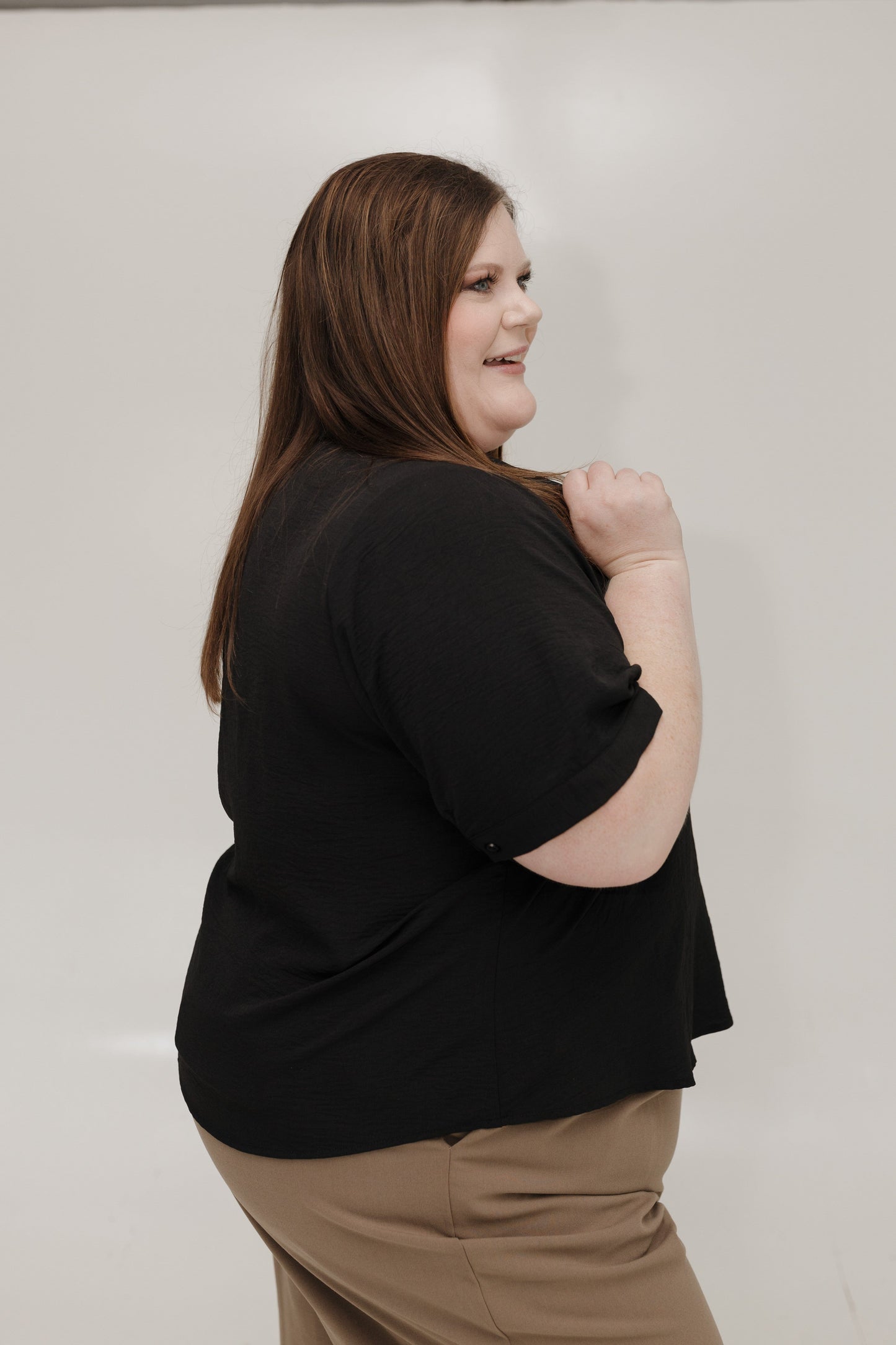 Woman wearing a black shirt and beige pants against a plain background