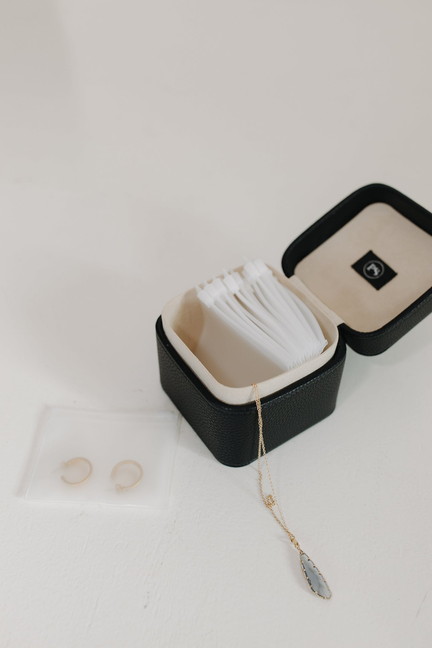 Black jewelry box with white interior, containing a necklace and two rings on a light gray background.