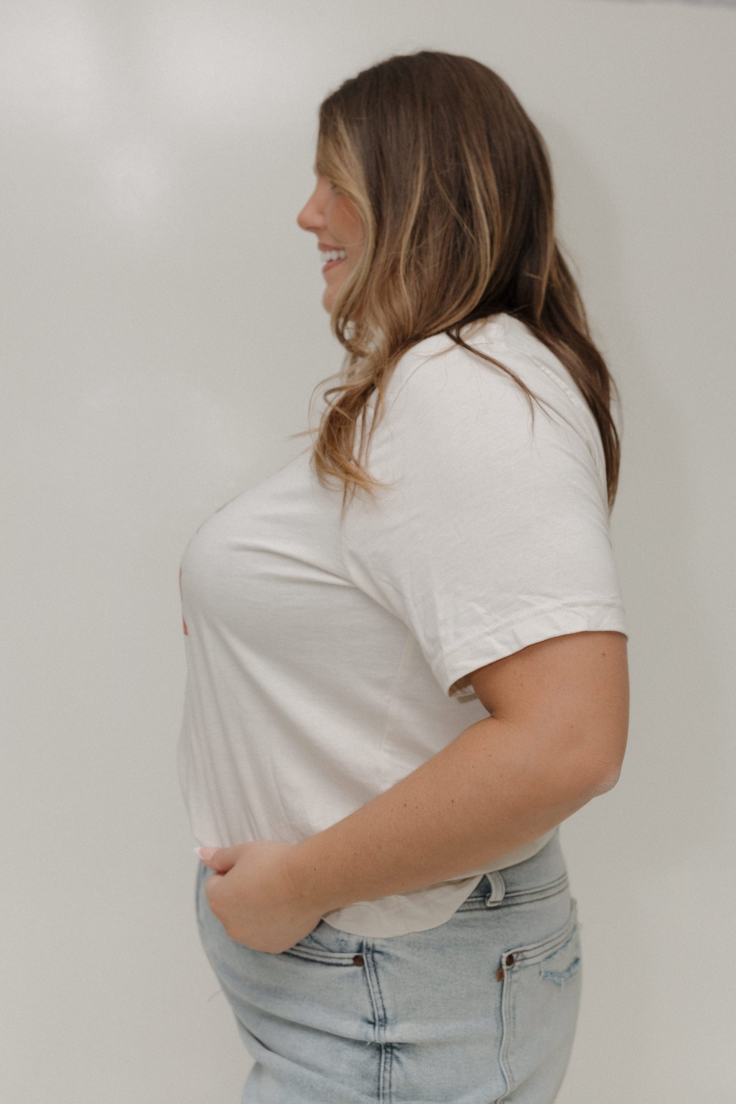 Woman wearing a white t-shirt and light blue jeans against a plain background