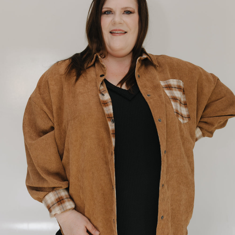 Woman wearing a brown jacket with plaid accents on a plain background
