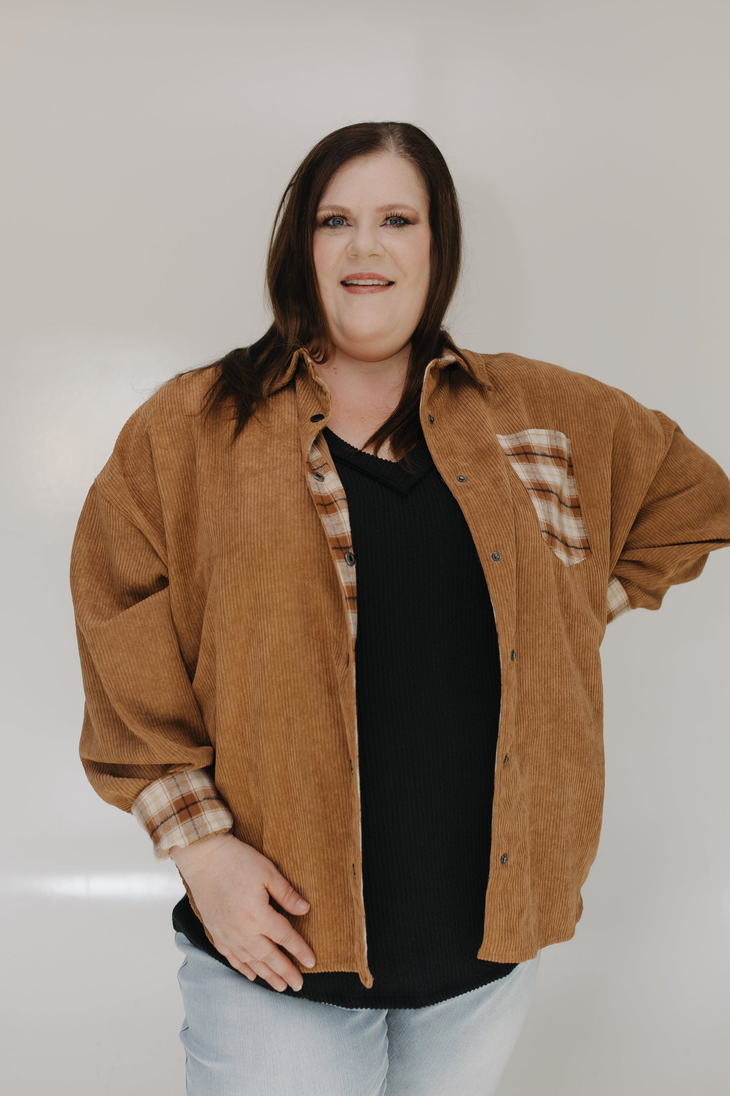 Woman wearing a brown jacket with plaid accents on a plain background