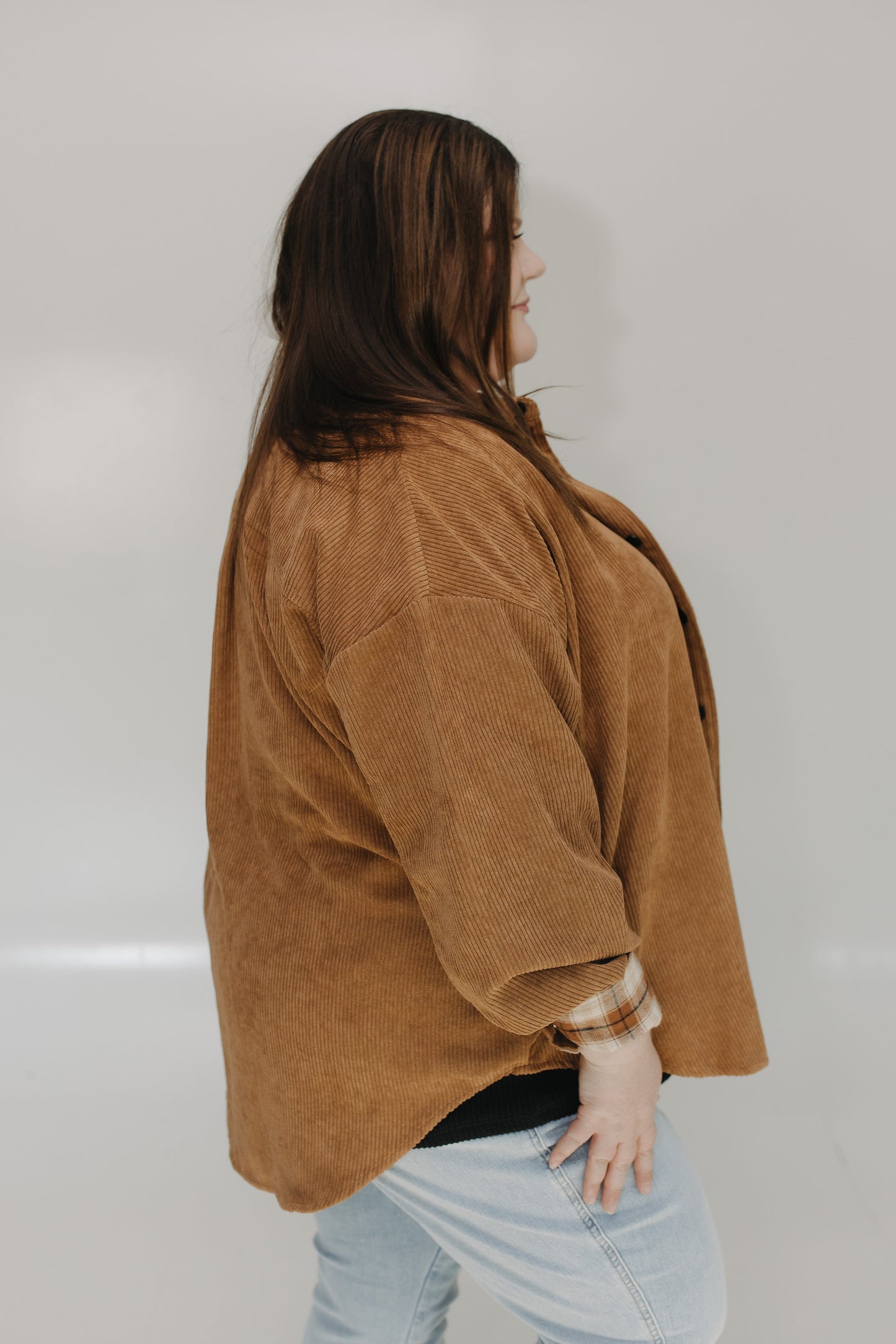 Person wearing a brown jacket and light blue jeans against a plain background